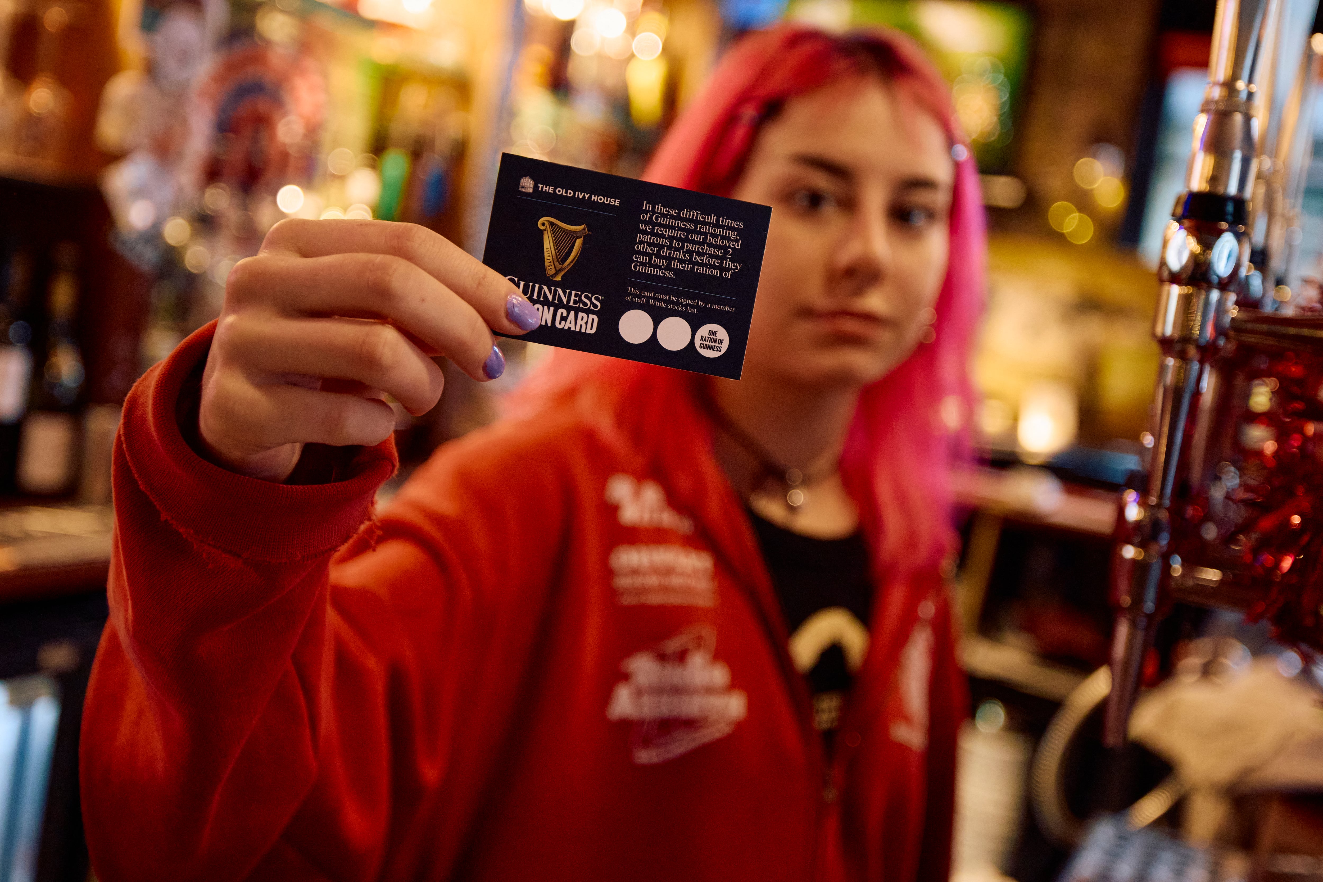 Kate Davidson, detrás de la barra de su pub en Londres, sostiene tarjetas de racionamiento de Guinness, implementadas ante la escasez de esta cerveza en Reino Unido.