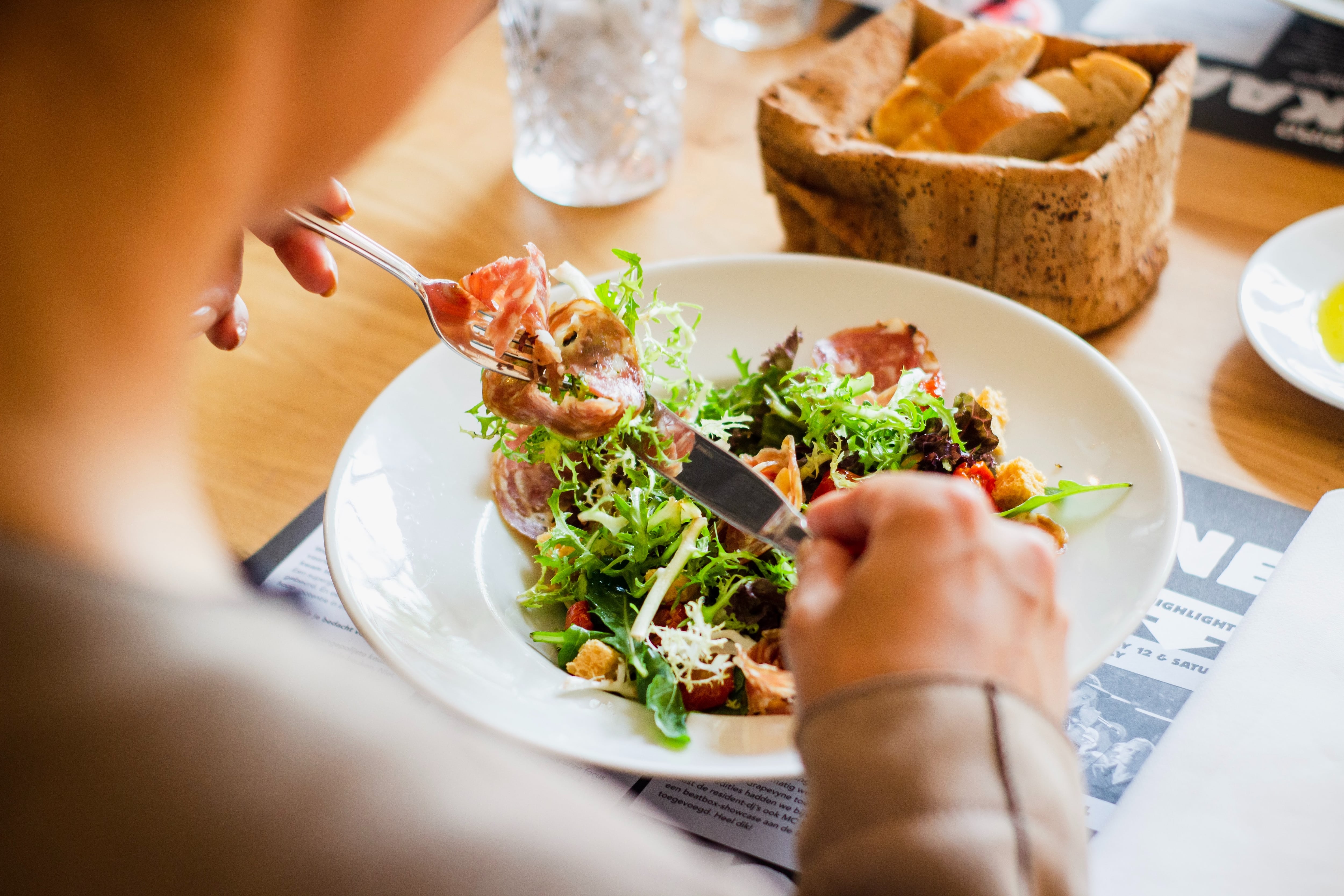 Persona a la que solo se le ve parte de la espalda come una ensalada.