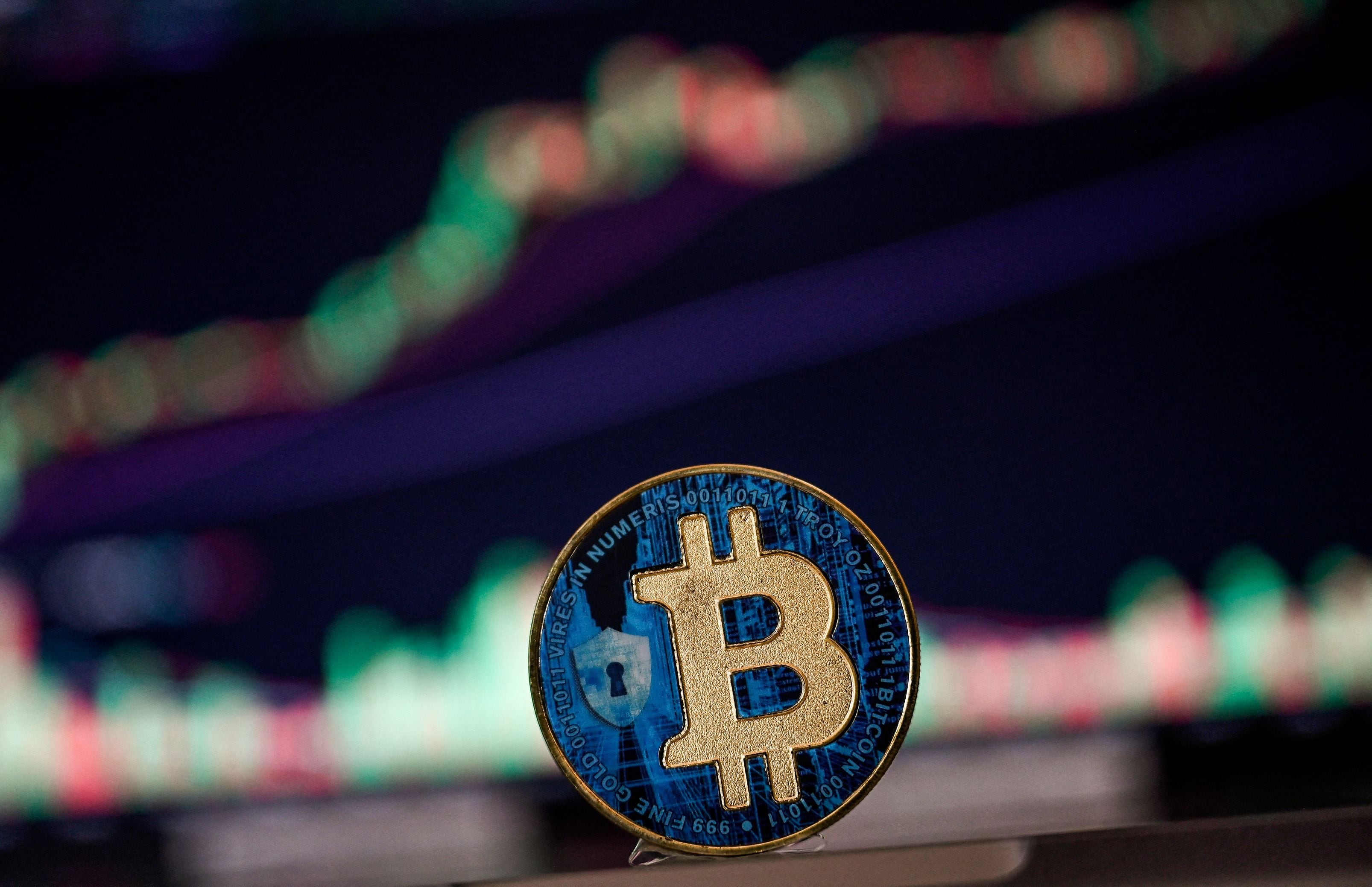 Moneda física de bitcóin en primer plano, con gráficos de mercado borrosos de fondo que reflejan la reciente subida de precio de la criptomoneda.