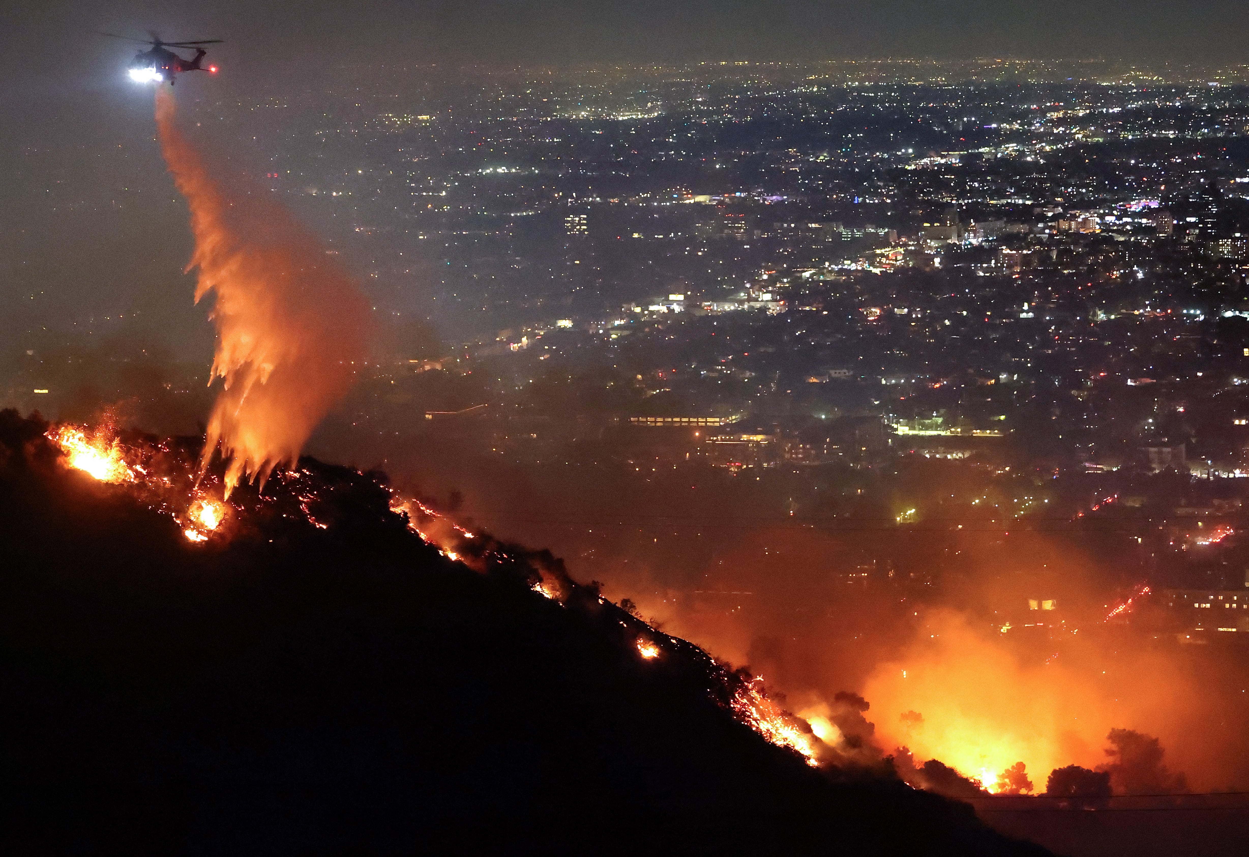 Un helicóptero de extinción de incendios arroja agua mientras el incendio Sunset arde en Hollywood Hills y se ordenaron evacuaciones en Los Ángeles, California.