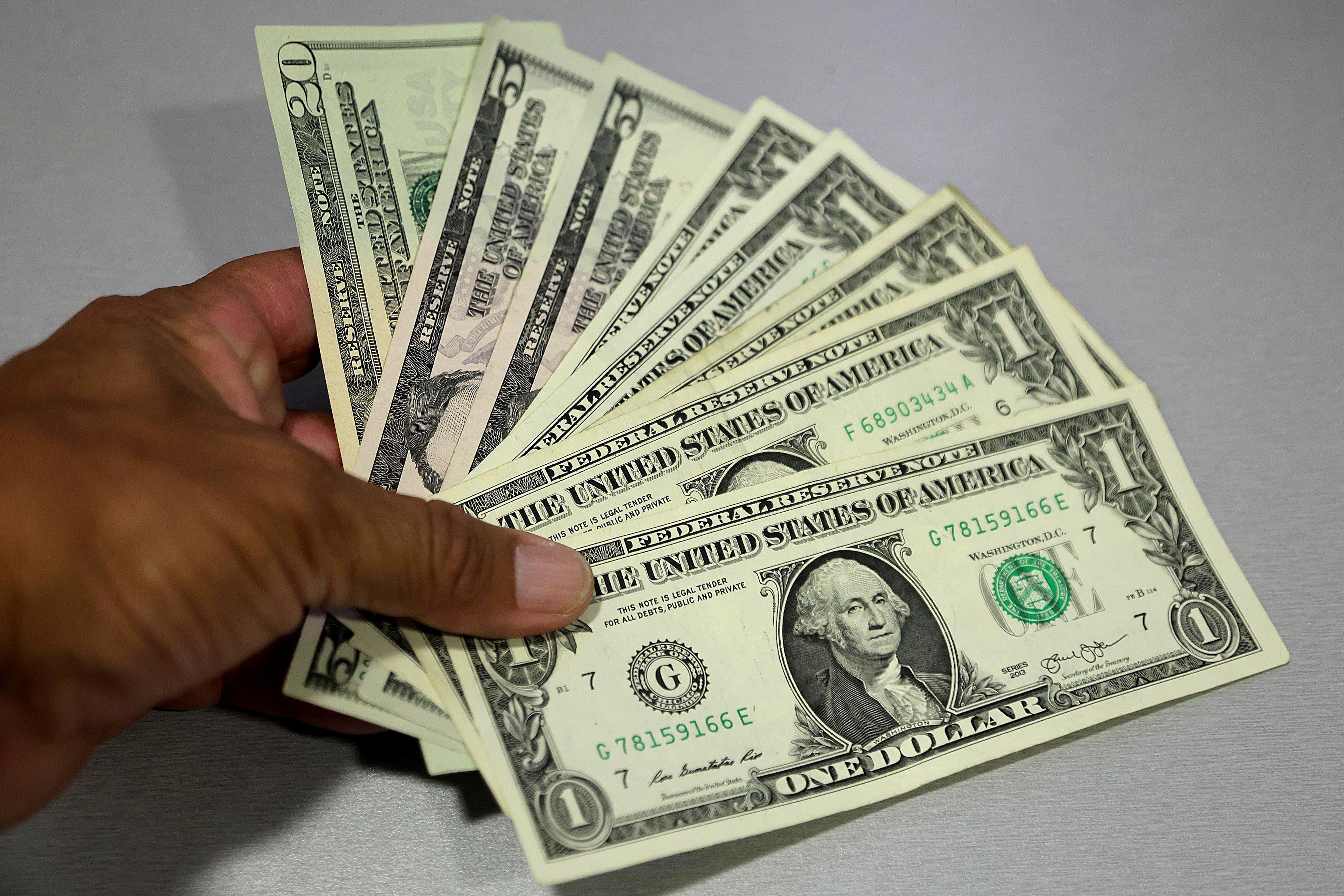 Mano sosteniendo varios billetes de dólar en efectivo, representando la oferta de divisas en Costa Rica y las proyecciones del Banco Central para 2025.