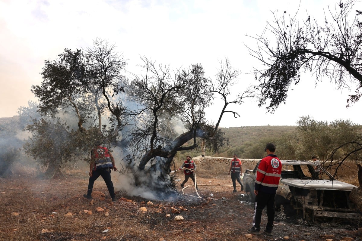 Voluntarios palestinos apagan el fuego en un olivo incendiado junto con un vehículo de propiedad palestina, presuntamente por colonos israelíes, cerca de la aldea de Turmus Ayya, al norte de Ramala, en la Cisjordania ocupada por Israel, el 16 de octubre de 2026.