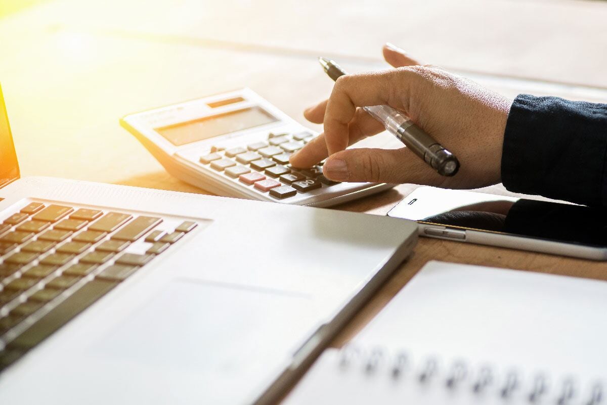 Mano de una persona usando una calculadora y una computadora portátil, representando el análisis de la recaudación fiscal en Costa Rica.