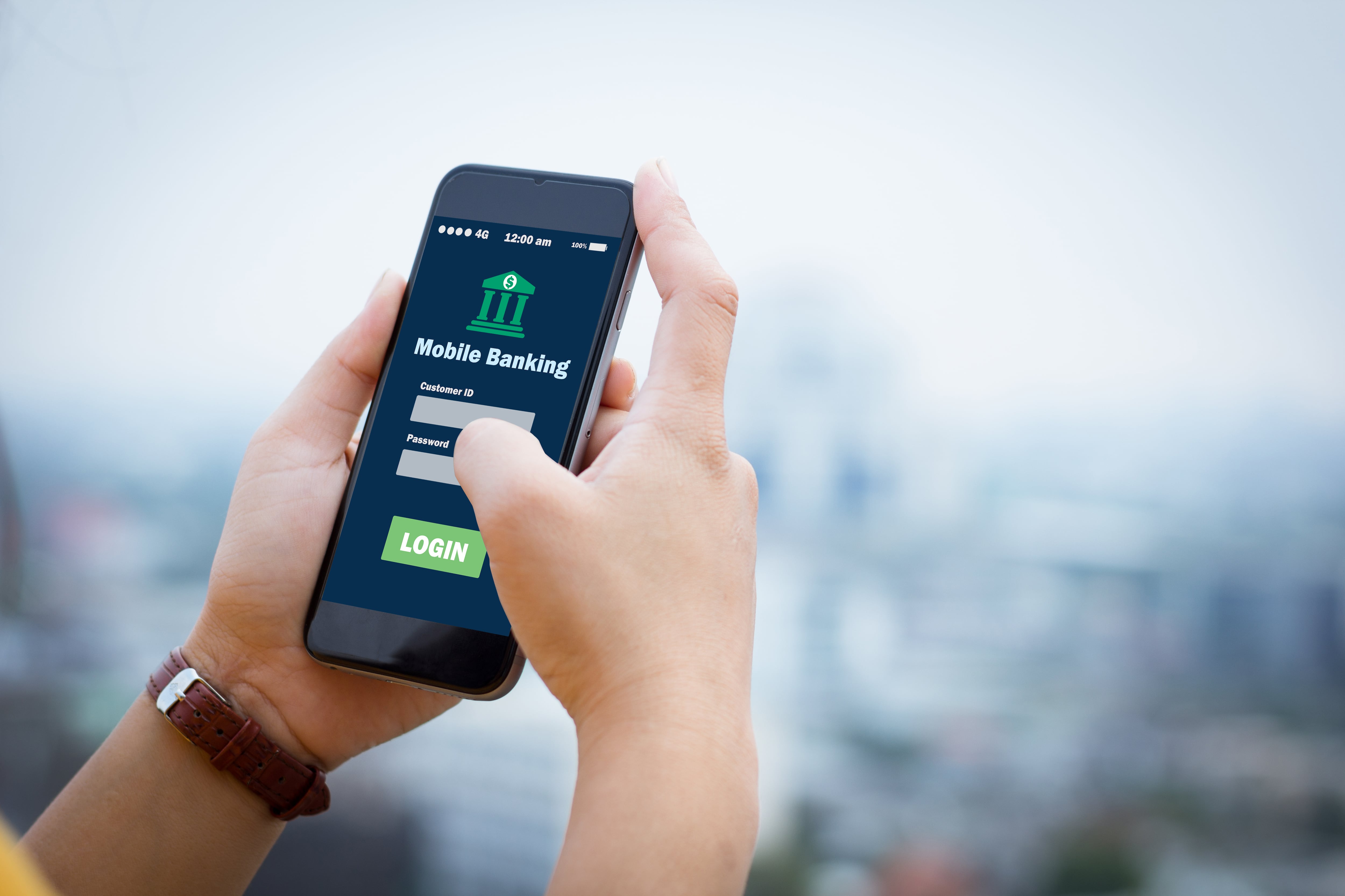 Primer plano de una mano sosteniendo un smartphone con una aplicación de banca móvil abierta, mostrando un formulario de inicio de sesión, sobre un fondo desenfocado.