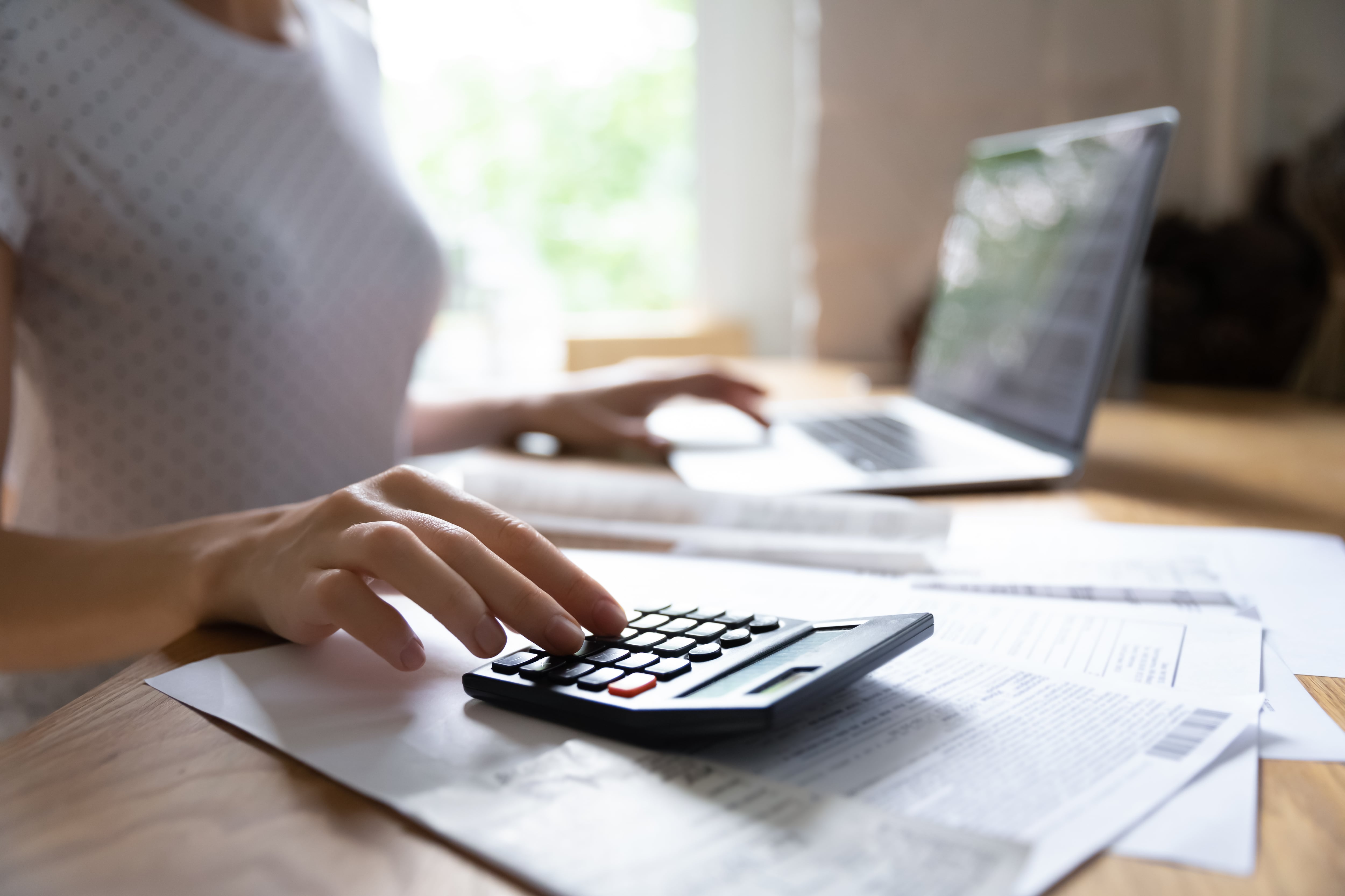 Mujer con calculadora y computadora portátil, haciendo cuentas