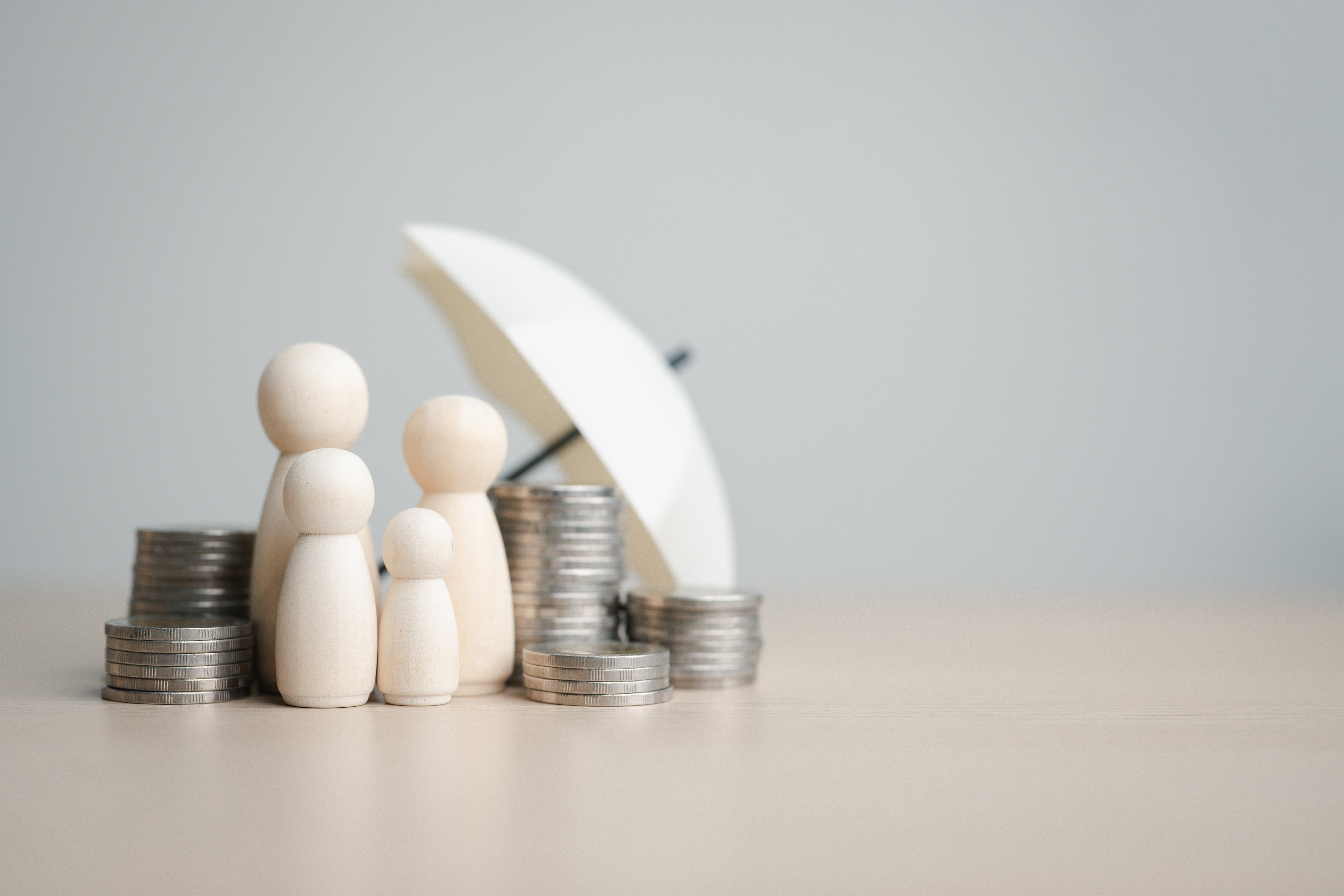 Figuras familiares con monedas y paraguas, que simbolizan la protección del seguro, la seguridad financiera, la planificación de ahorros y la cobertura de vida para la estabilidad futura. Protección del consumidor financiero.