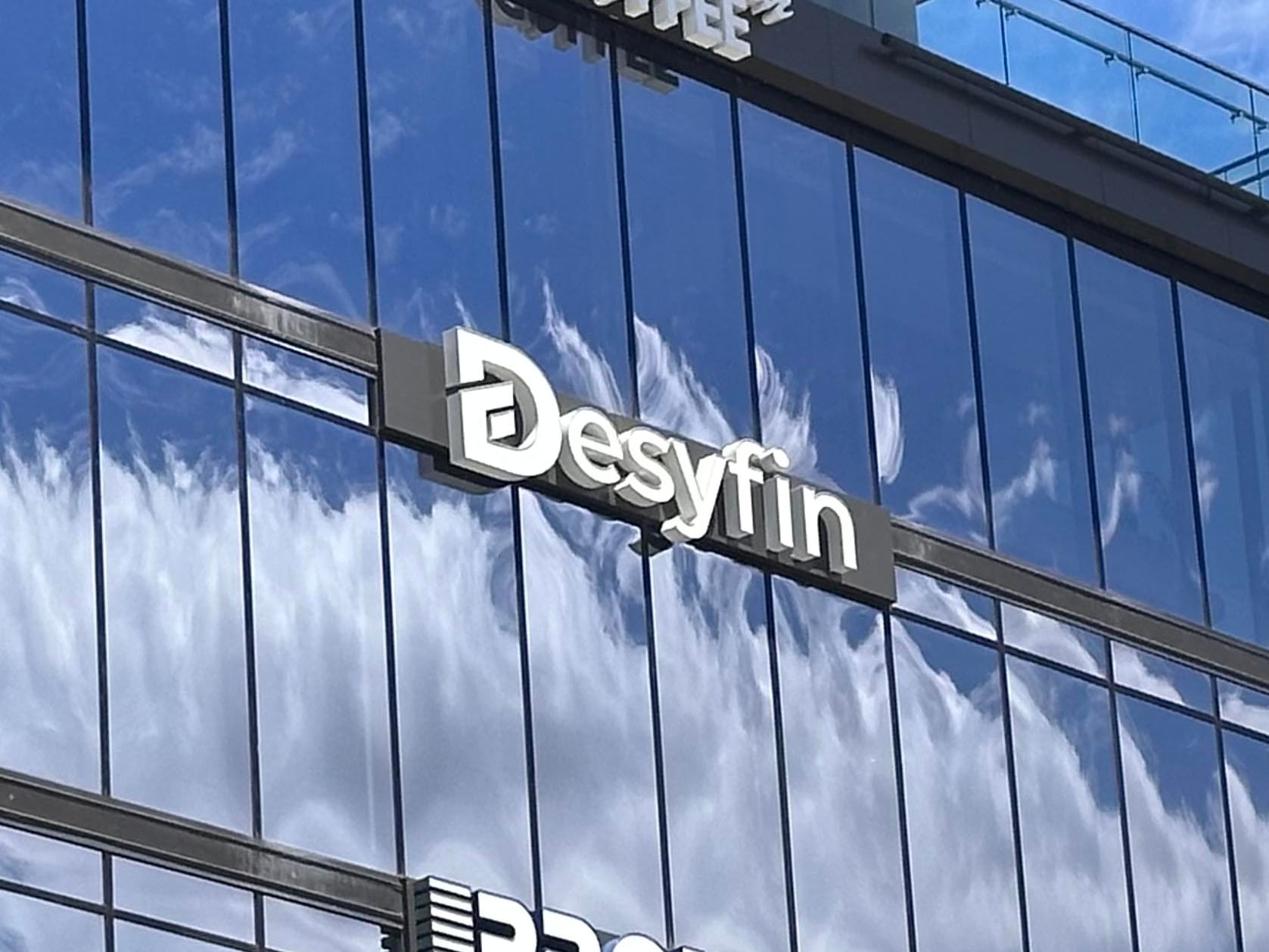 Edificio de la Financiera Desyfin con logotipos visibles y cielo reflejado en las ventanas, en medio de una investigación.