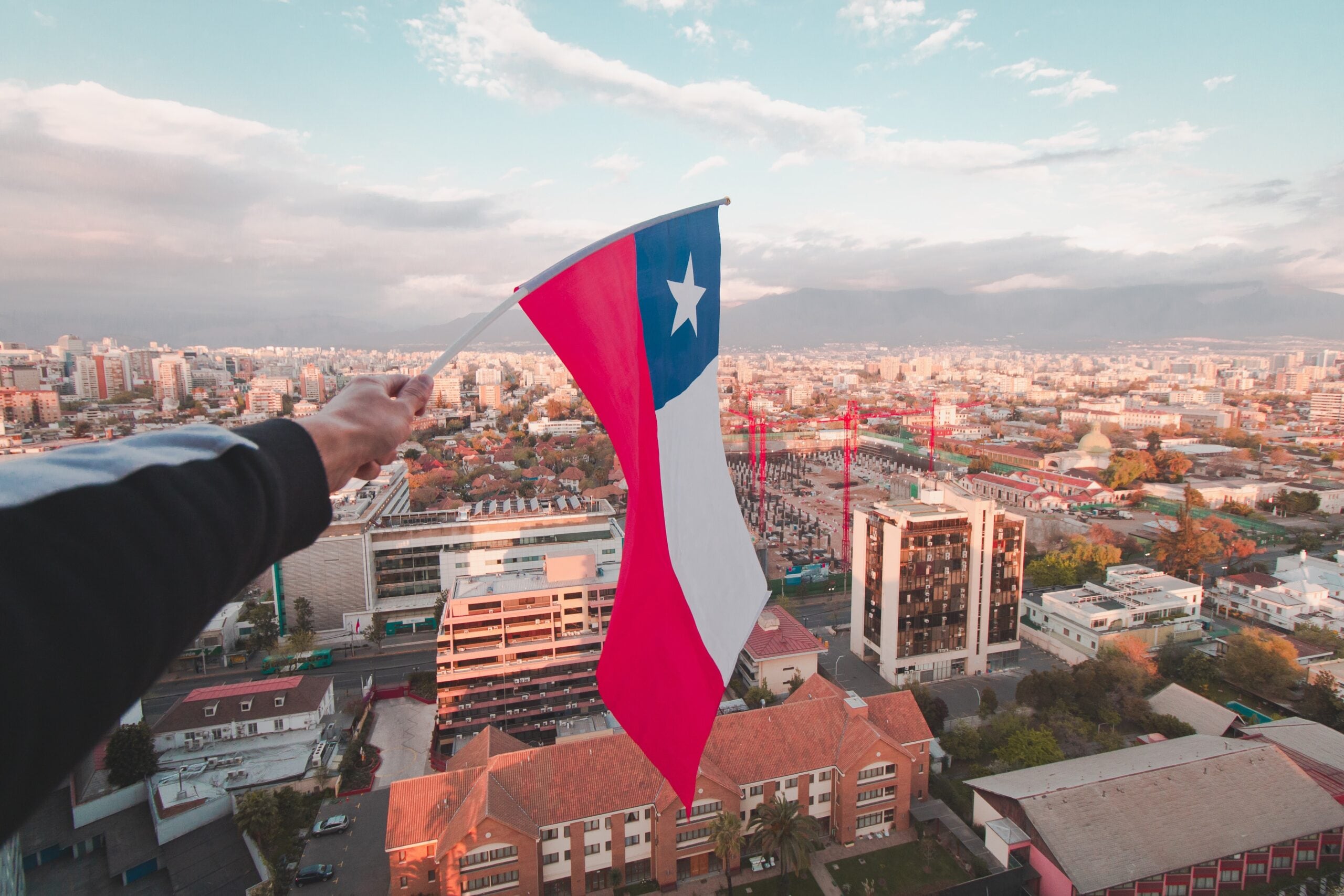 vista panorámica de la ciudad de Santiago de Chile con la bandera nacional, conocida como "La Estrella Solitaria", ondeando en primer plano.