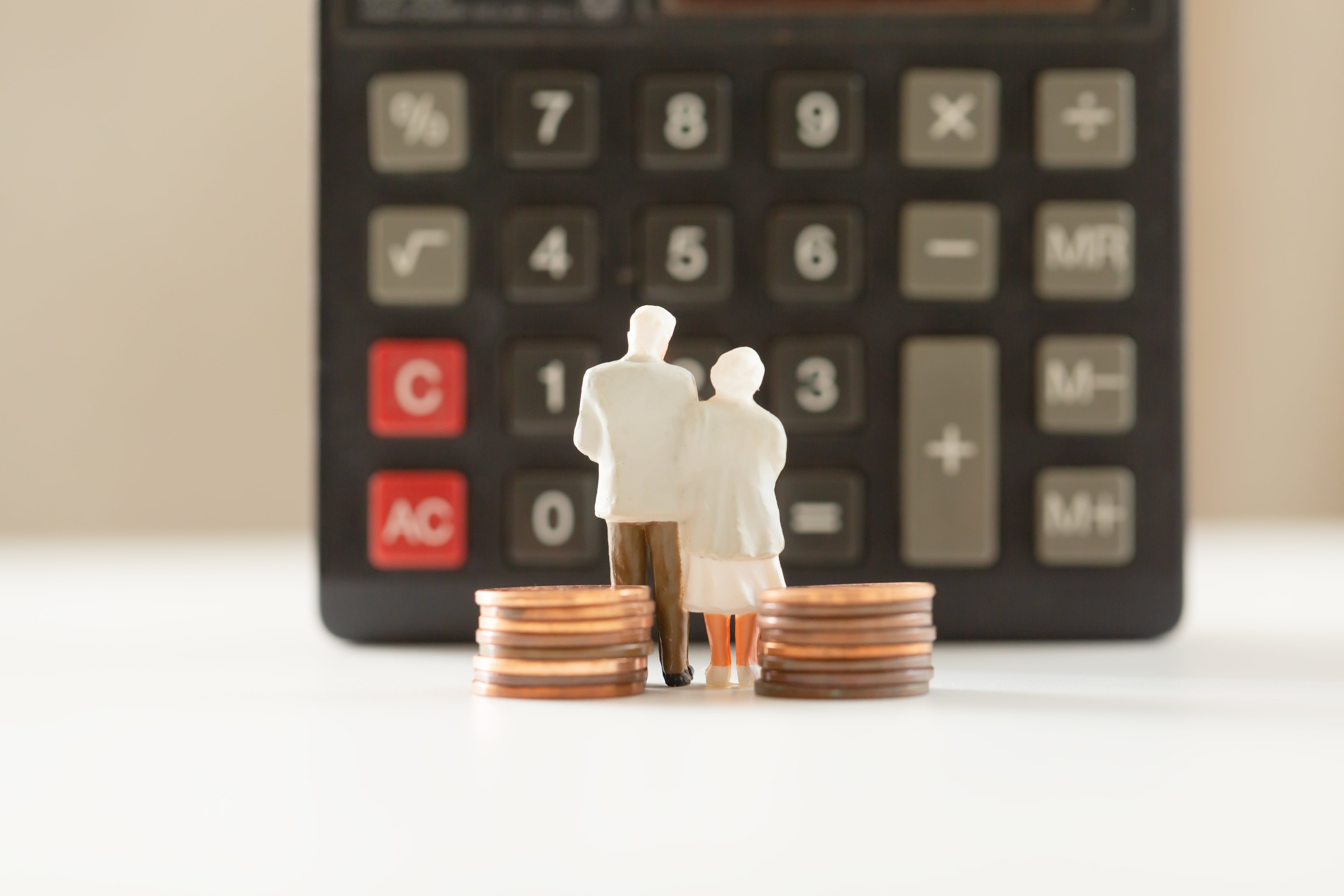 en la imagen, dos figuras de adultos mayores frente a una calculadora
