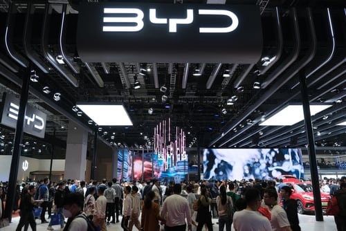 Stand de la empresa china de autos eléctricos BYD en un evento automotriz, con múltiples visitantes observando la exhibición.