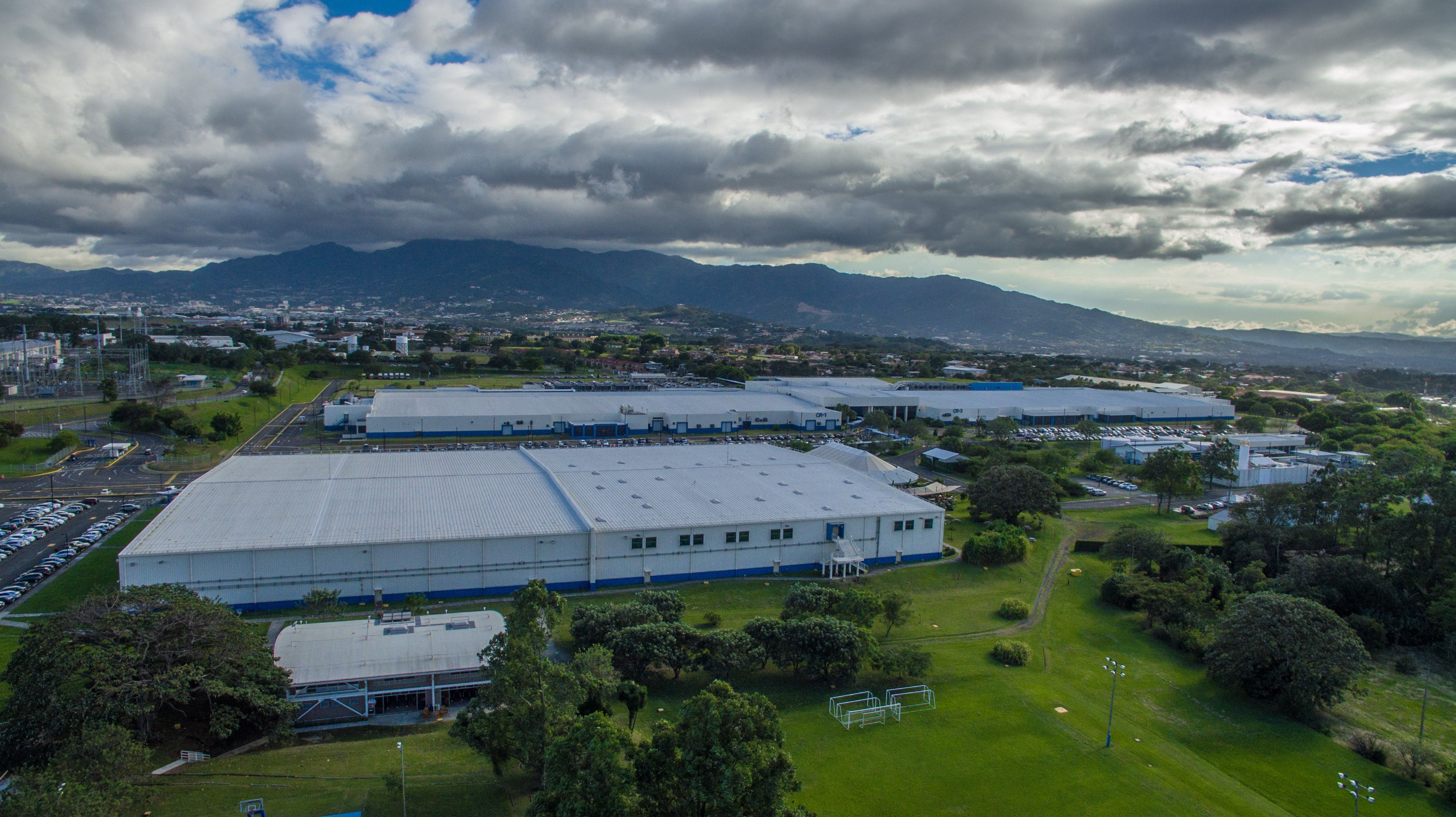Vista aérea de la planta de Intel en Belén de Heredia, Costa Rica, rodeada de áreas verdes, con montañas al fondo, bajo un cielo parcialmente nublado.