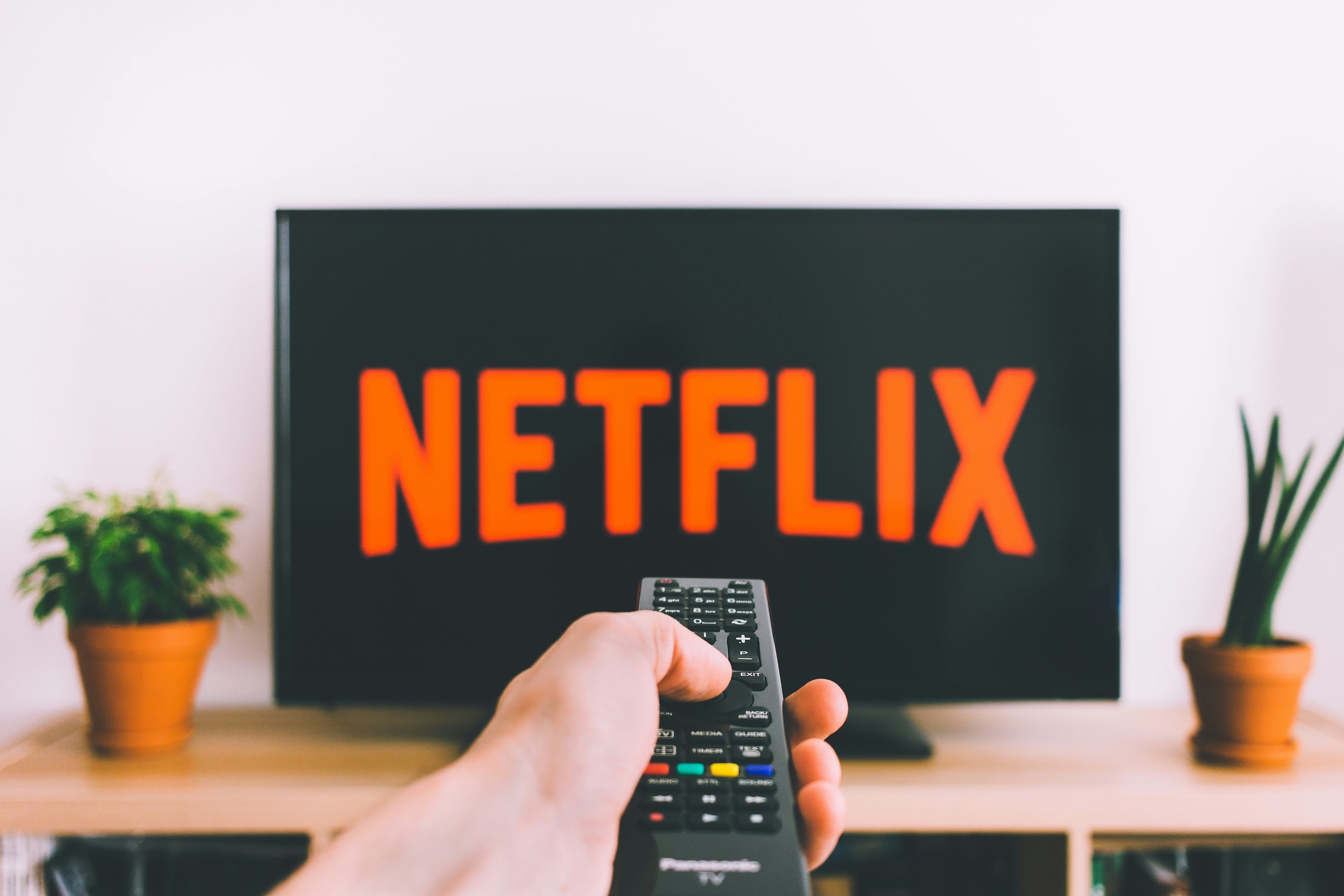 Mano sosteniendo un control remoto frente a una pantalla con el logo de Netflix, representando el uso de la plataforma de streaming que ha alcanzado 300 millones de suscriptores.