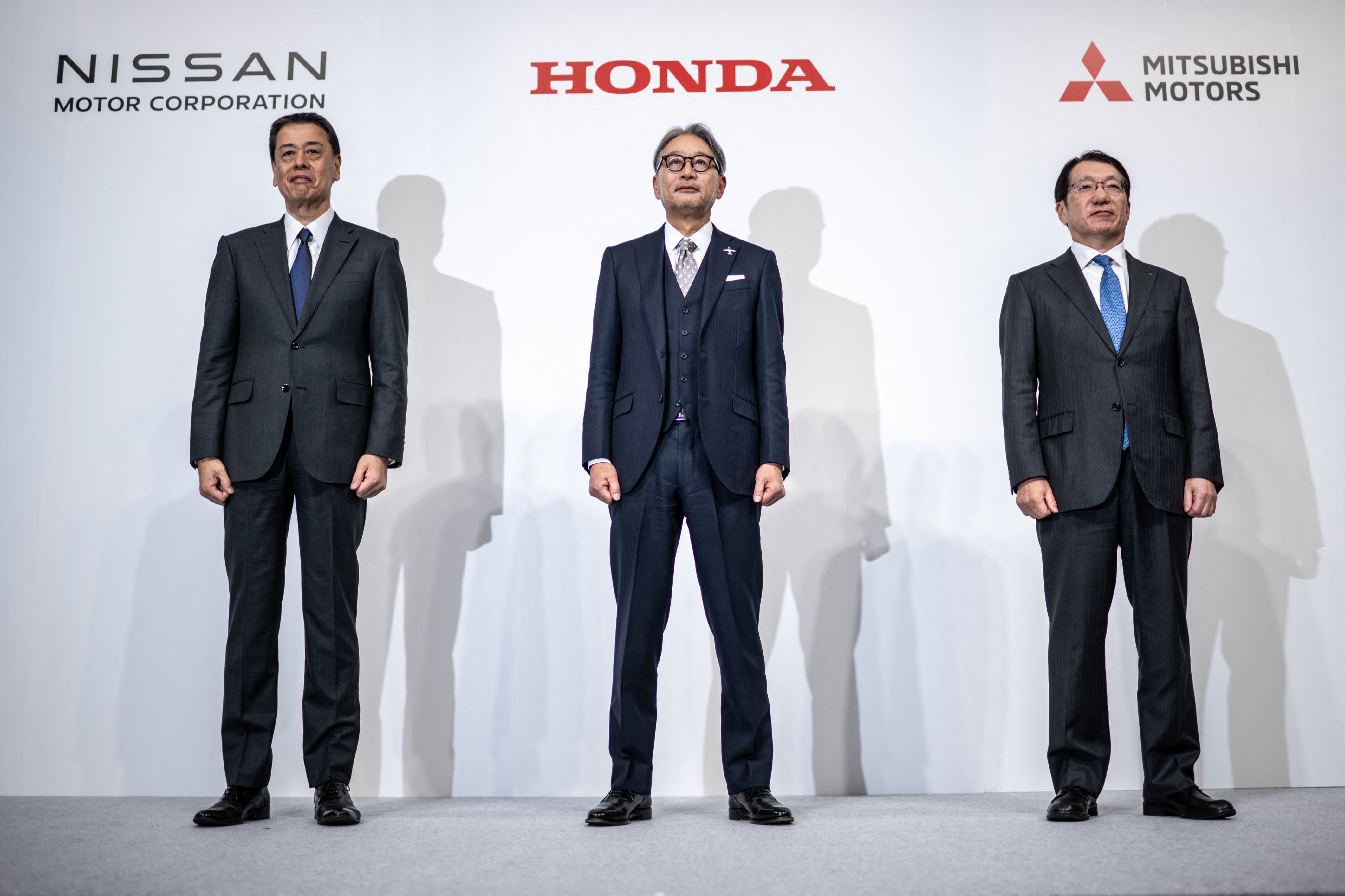 Tres hombres asiáticos de pie, cada uno debajo de los logos de Nissan, Honda y Mitsubishi.