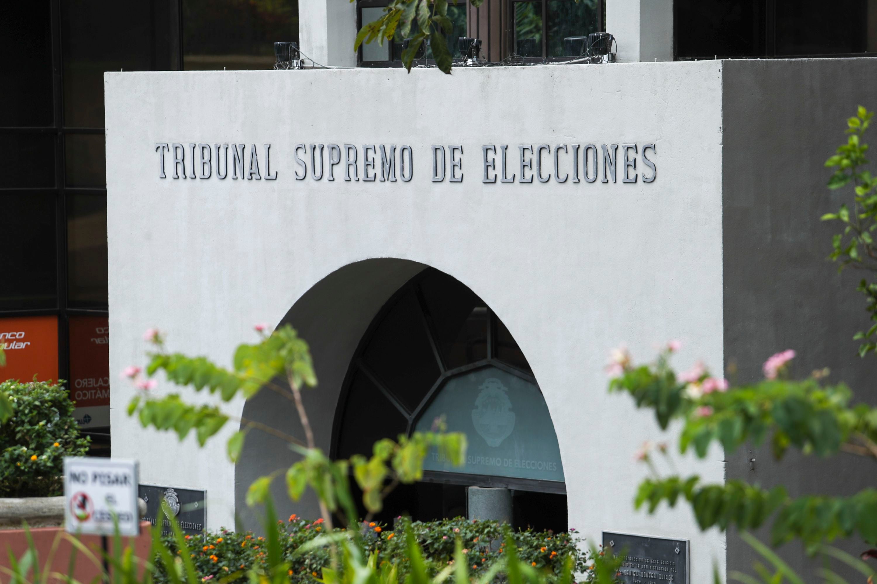 Fachada del edificio del Tribunal Supremo de Elecciones (TSE) en Costa Rica, con su nombre inscrito en la parte superior de la entrada, rodeada de vegetación.