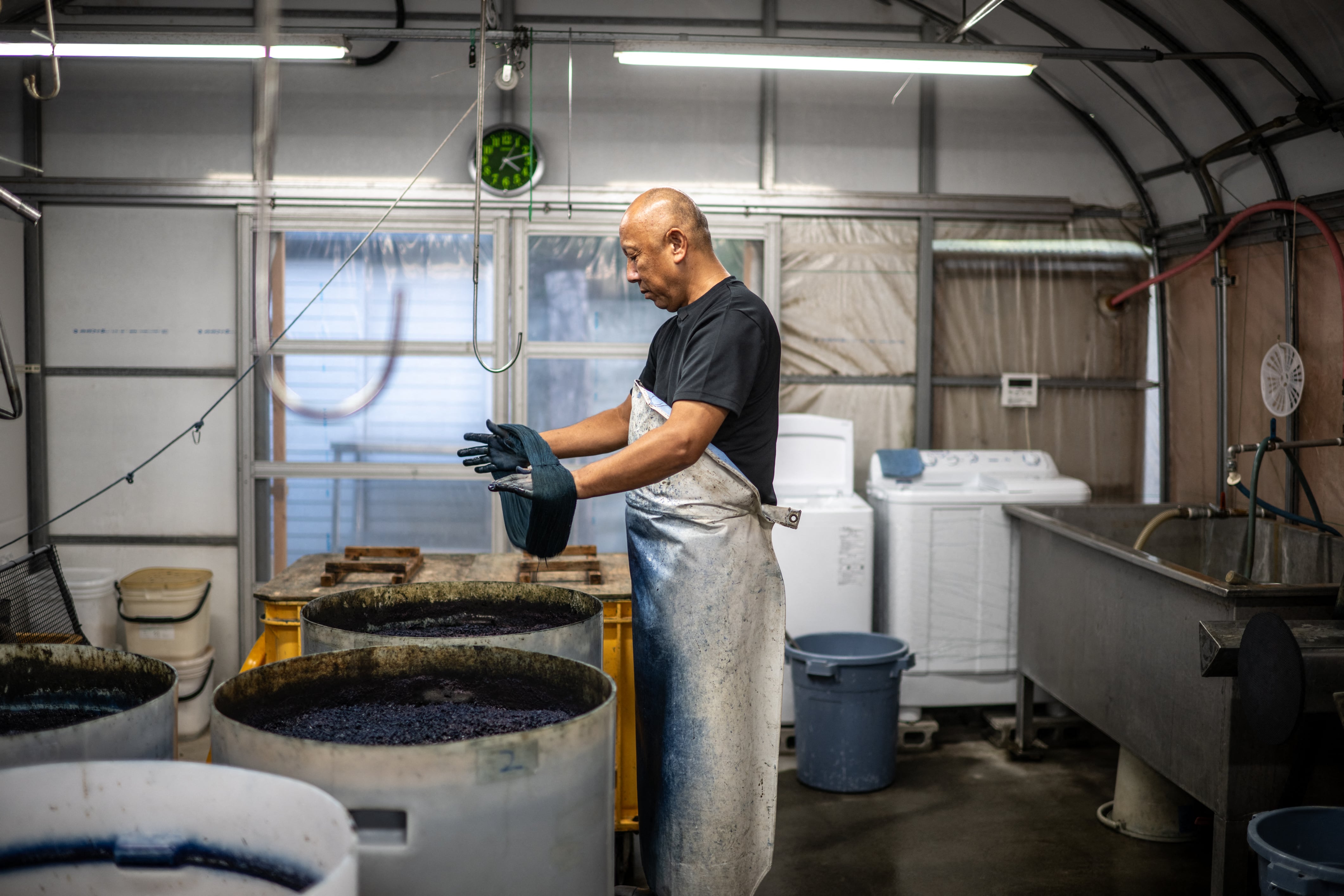 Hombre asiático de pie sostiene hilos de algodón en el proceso de teñido para la elaboración artesanal de jeans en Japón