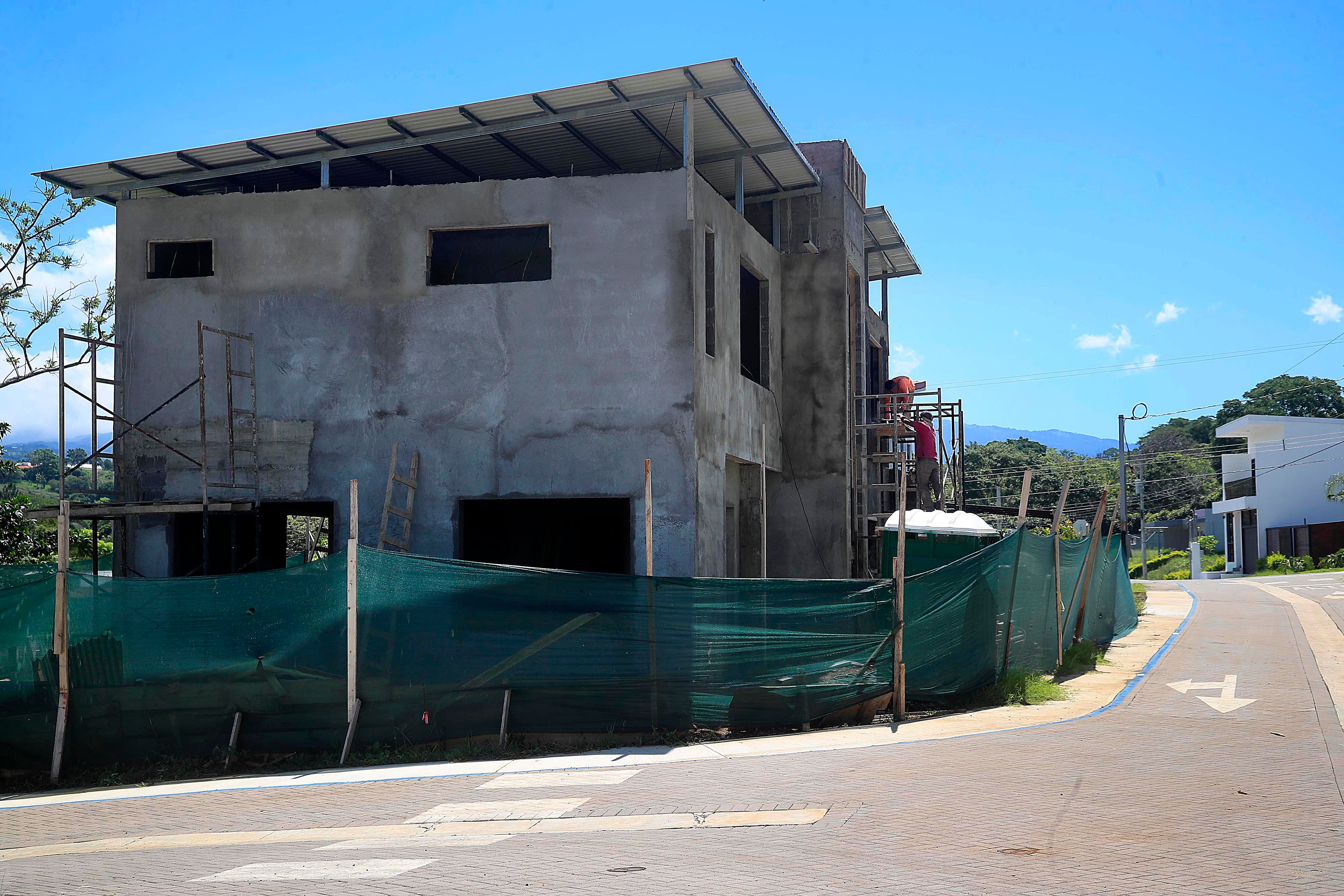 Vista de una vivienda en construcción en Grecia, Alajuela, con andamios y cercas verdes en el perímetro, representando el crecimiento del sector inmobiliario en la región.