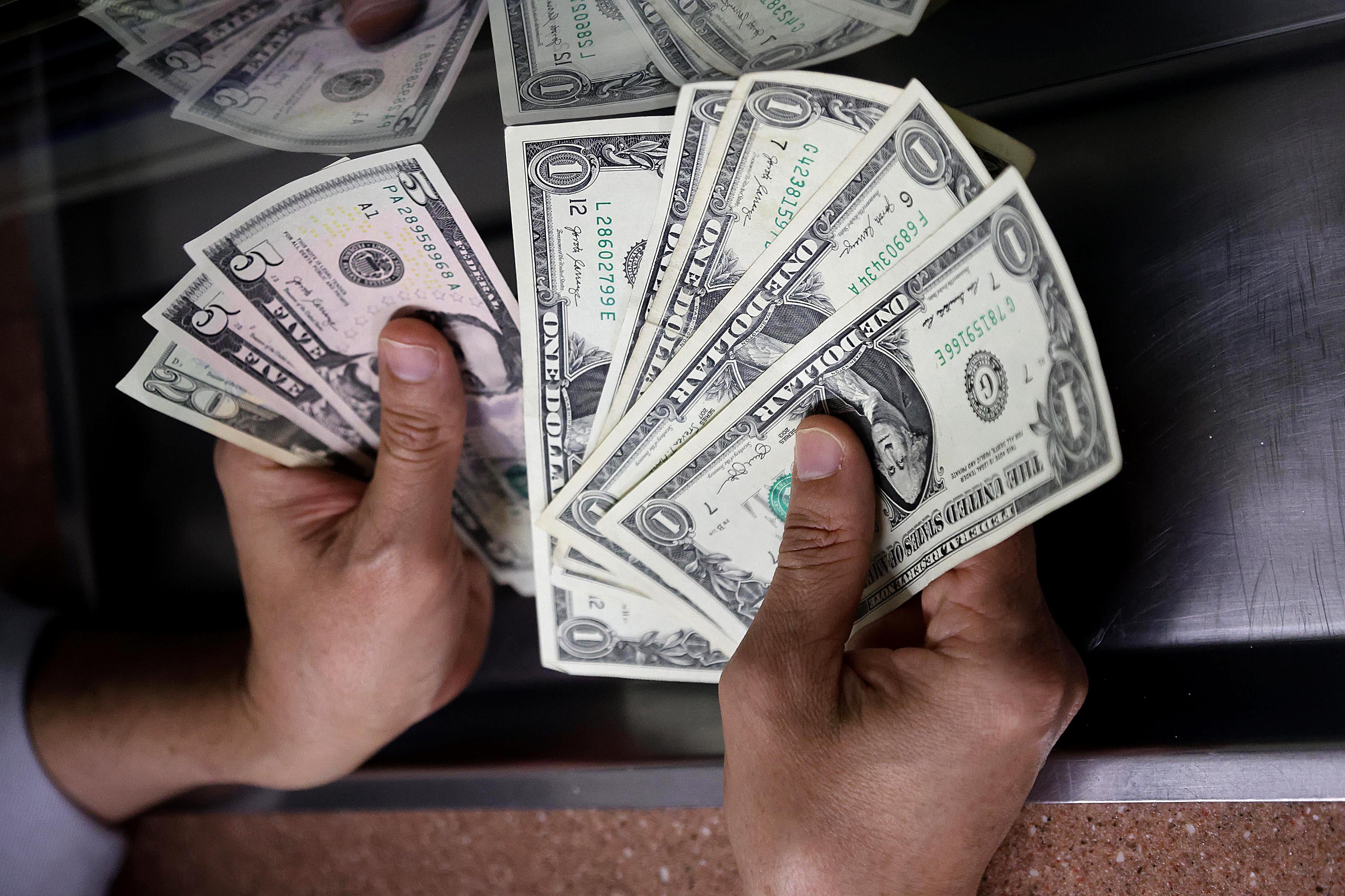 Una persona contando billetes de dólar estadounidense en un mostrador.