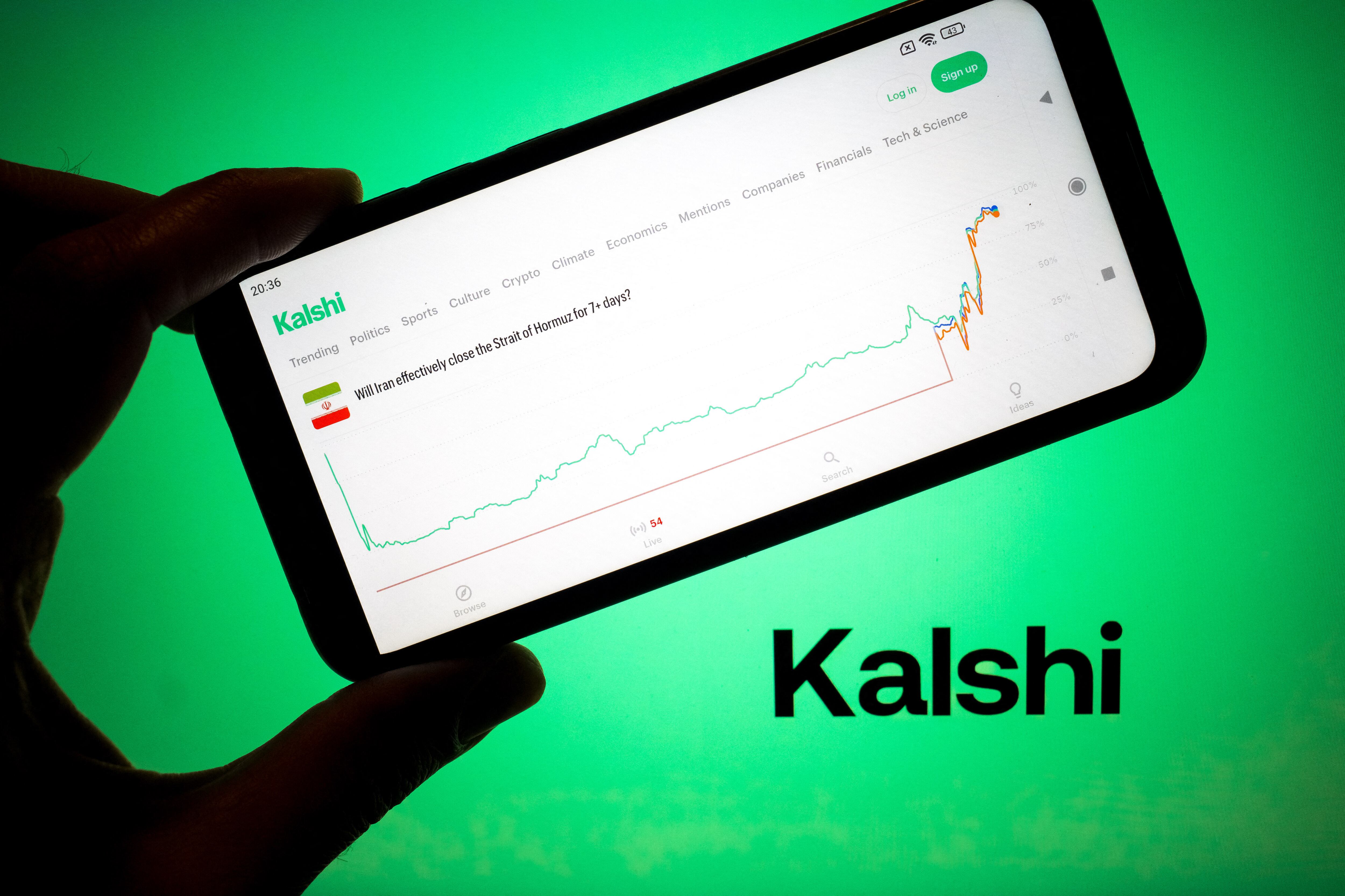 El mercado Kalshi con la frase "¿Cerrará Irán el estrecho de Ormuz durante más de 7 días?" aparece en la pantalla de un teléfono inteligente, con el logotipo de Kalshi en la pantalla de una computadora portátil al fondo, en esta ilustración fotográfica tomada en Chania, Grecia, el 9 de marzo de 2026.