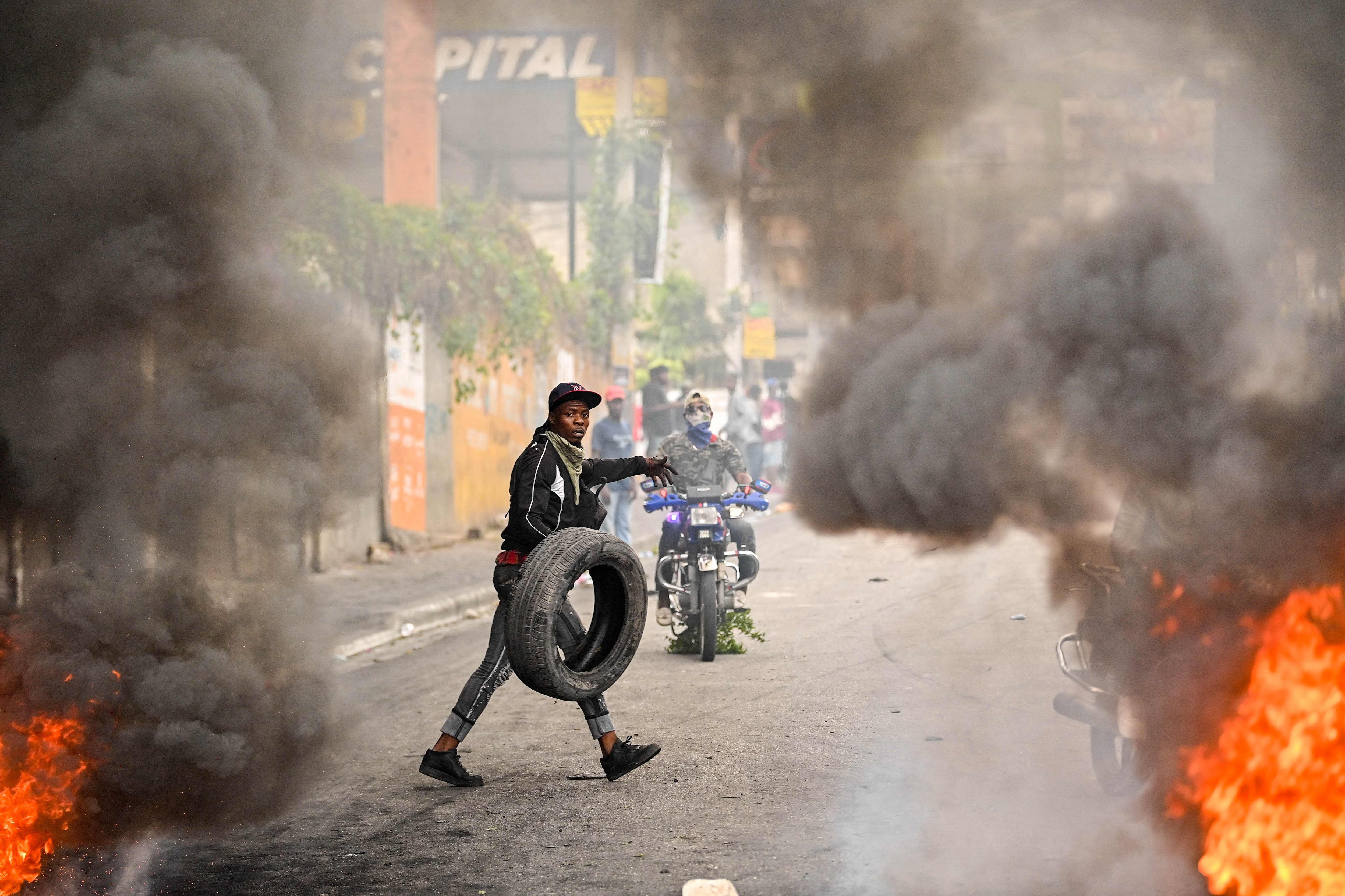 Un manifestante haitiano sostiene una llanta mientras el fuego y el humo llenan una calle en medio de protestas en Haití.