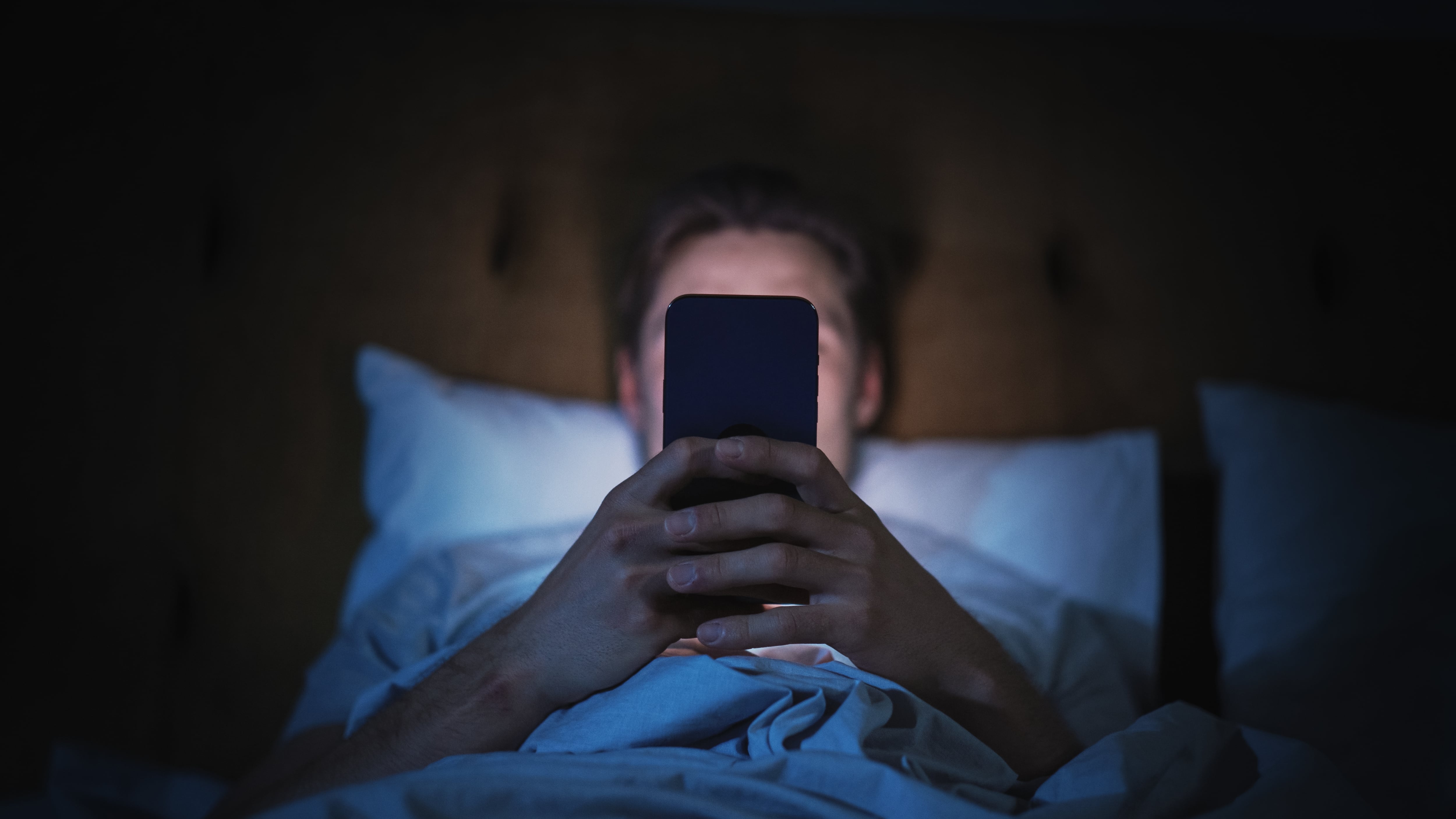 Hombre en la cama, a oscuras, mirando su teléfono celular