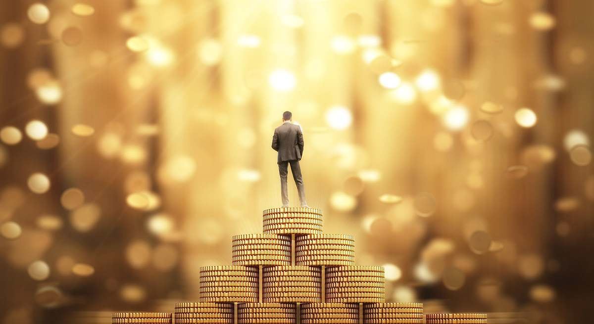 Ser millonario o multimillonario, simbolizado por una figura humana de pie sobre una pila de monedas de oro con un fondo borroso y brillante.