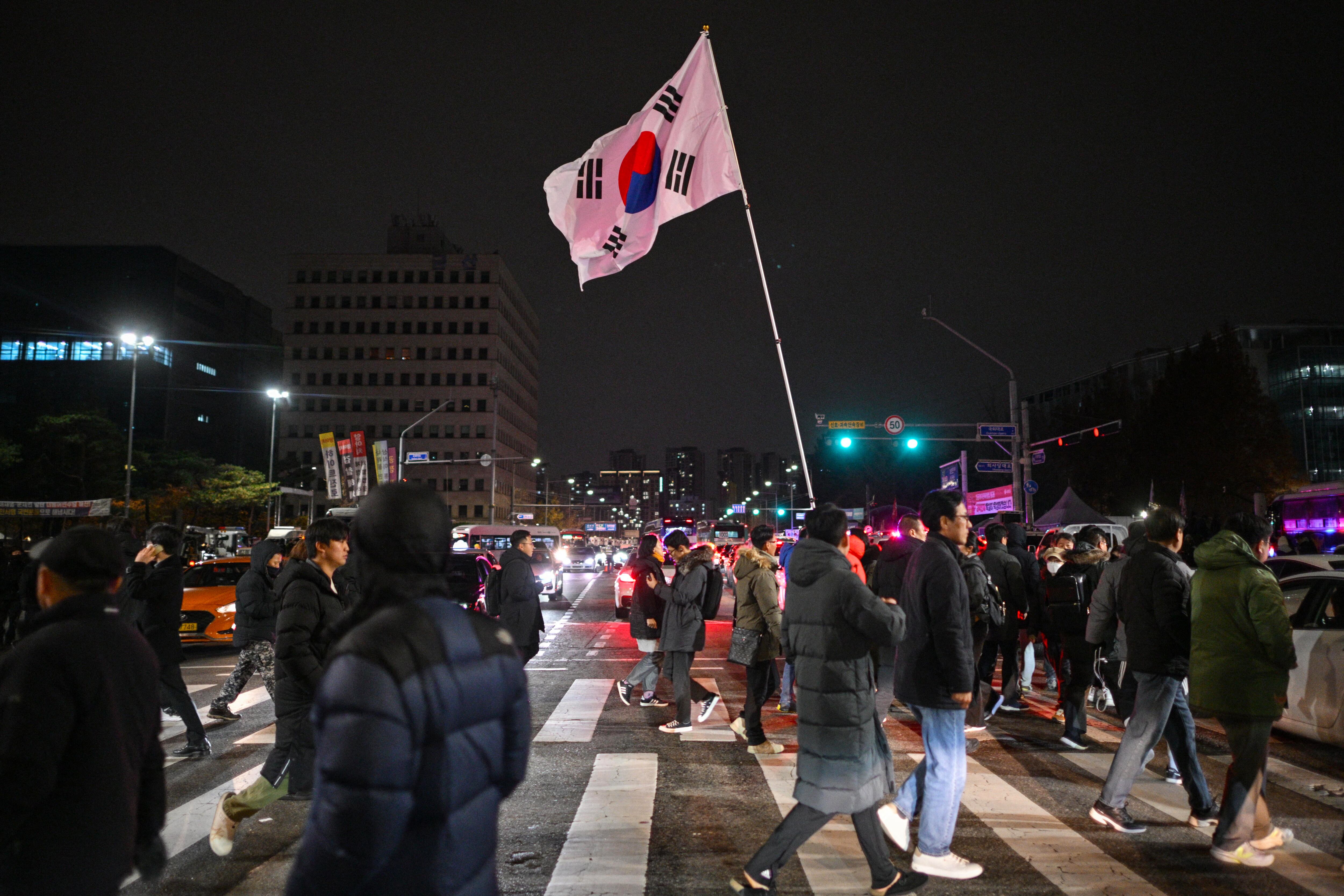 Hombre sostiene la bandera de Corea del Sur frente a la Asamblea Nacional en Seúl, el 4 de diciembre de 2024, tras la declaración de ley marcial por Yoon Suk Yeol.