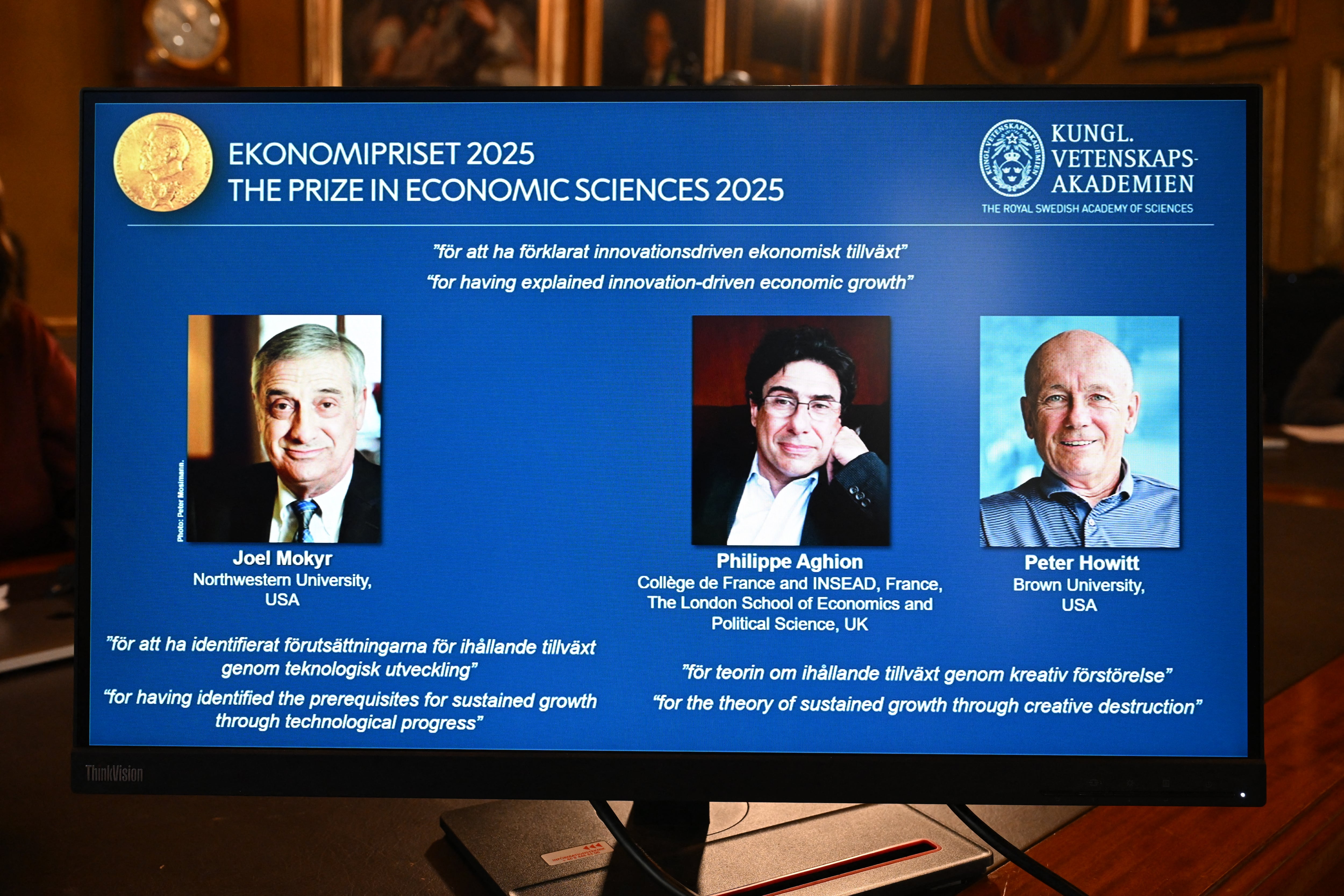 Una pantalla muestra los retratos de los ganadores del Premio Nobel de Economía 2025 (de izq. a der.): Joel Mokyr, Philippe Aghion y Peter Howitt, durante el anuncio de los ganadores del Premio Nobel de Economía 2025, el Premio Sveriges Riksbank en Ciencias Económicas en memoria de Alfred Nobel, en la Real Academia Sueca de Ciencias en Estocolmo, Suecia, este 13 de octubre. Fotografía: