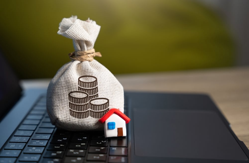 Una bolsa de dinero y una casa a escala sobre un teclado de una computadora portátil