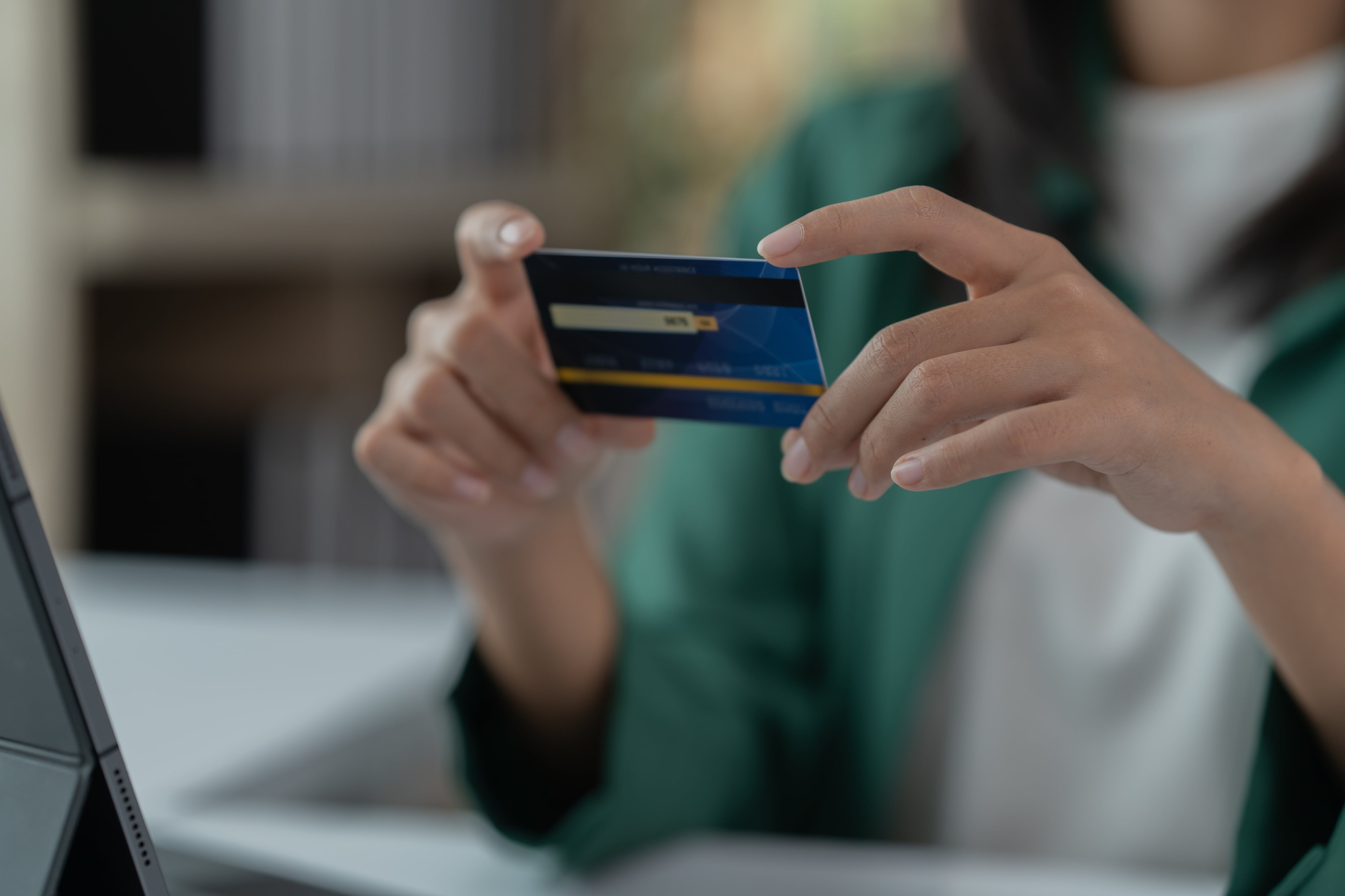 Manos de una persona sosteniendo una tarjeta de crédito frente a una computadora portátil, representando transacciones financieras o compras en línea.