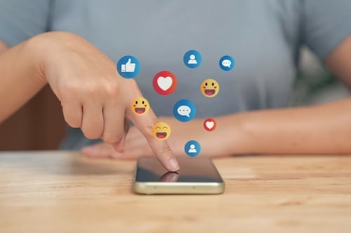 Persona usando un móvil para enviar emoticones, representando la comunicación digital en redes sociales.