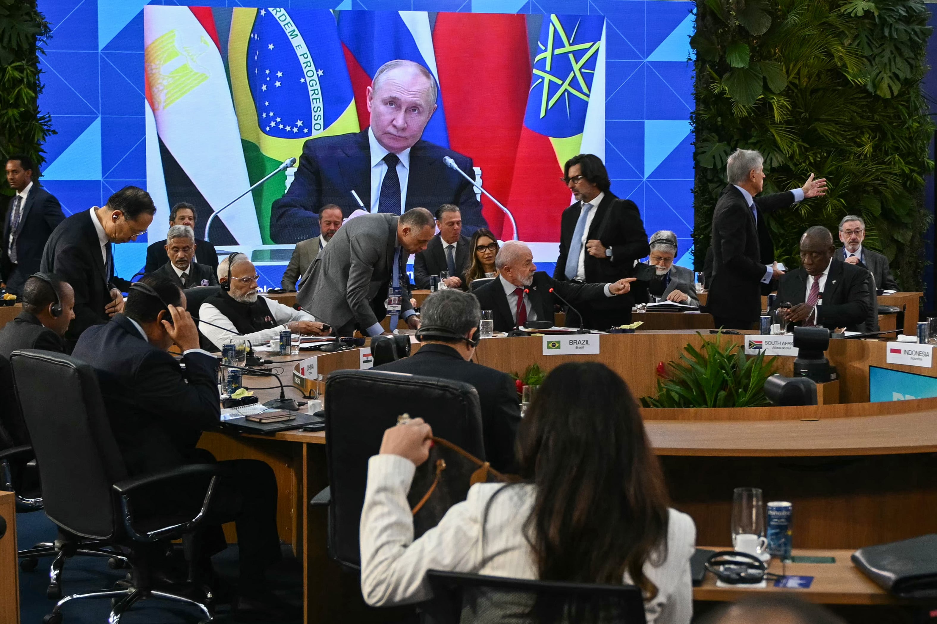 El presidente de Rusia, Vladimir Putin, aparece proyectado en una pantalla durante la primera sesión plenaria de la cumbre del BRICS en Río de Janeiro, Brasil, el 6 de julio de 2025. Se espera que los líderes del BRICS, reunidos en Río de Janeiro este domingo, denuncien los aranceles comerciales “indiscriminados” del presidente estadounidense Donald Trump, calificándolos de ilegales y perjudiciales para la economía global. (Foto de Mauro PIMENTEL / AFP)
