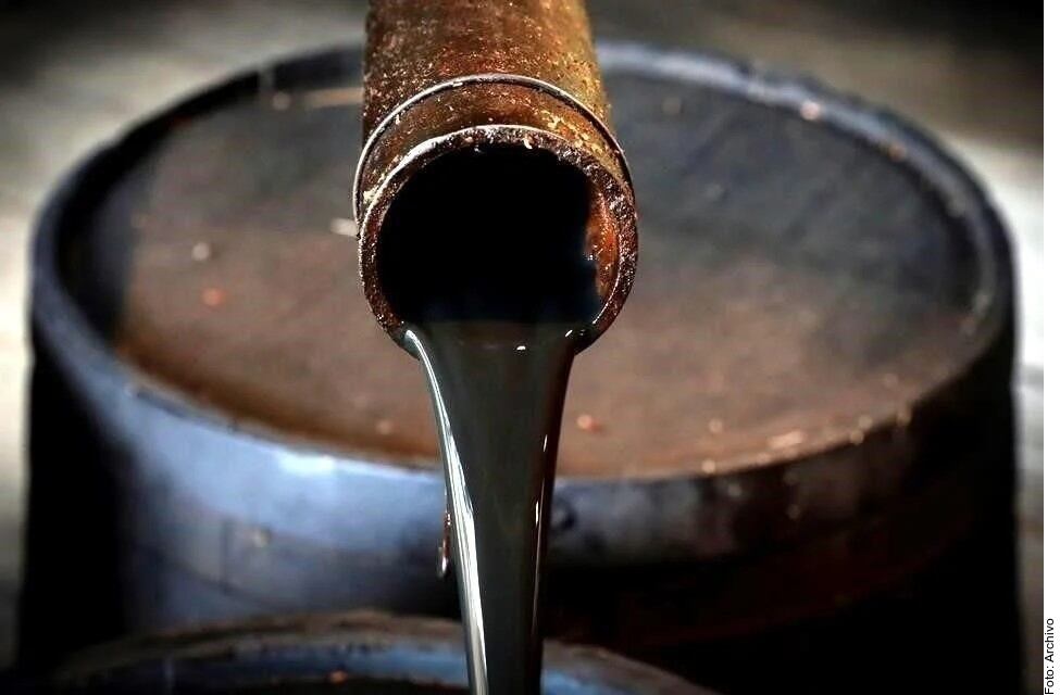 Primer plano de una tubería metálica de la que fluye petróleo crudo oscuro hacia un recipiente de almacenamiento durante una operación de la industria petrolera.