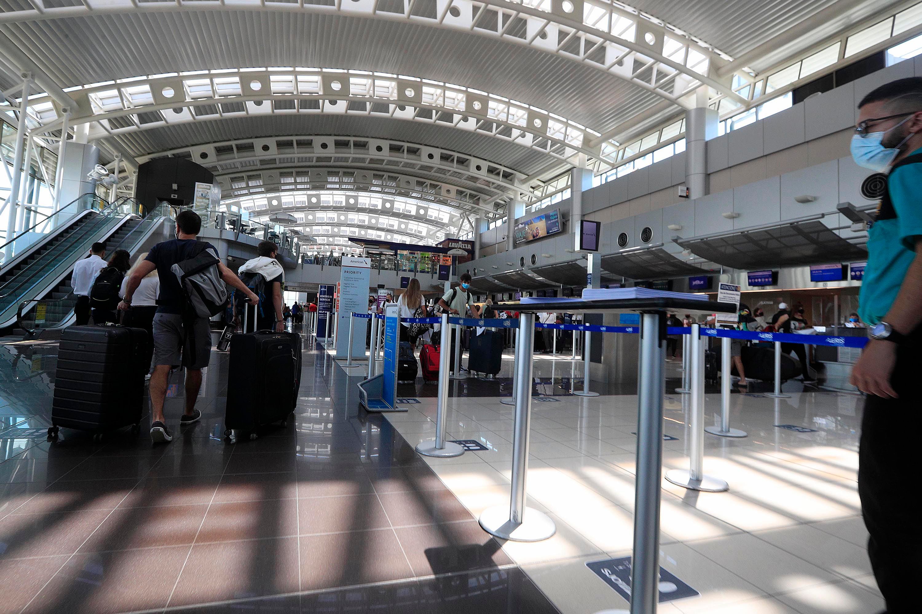 Pasajeros caminan en la terminal del Aeropuerto Internacional Juan Santamaría, iluminada con luz natural, mientras esperan realizar procesos de check-in o migración