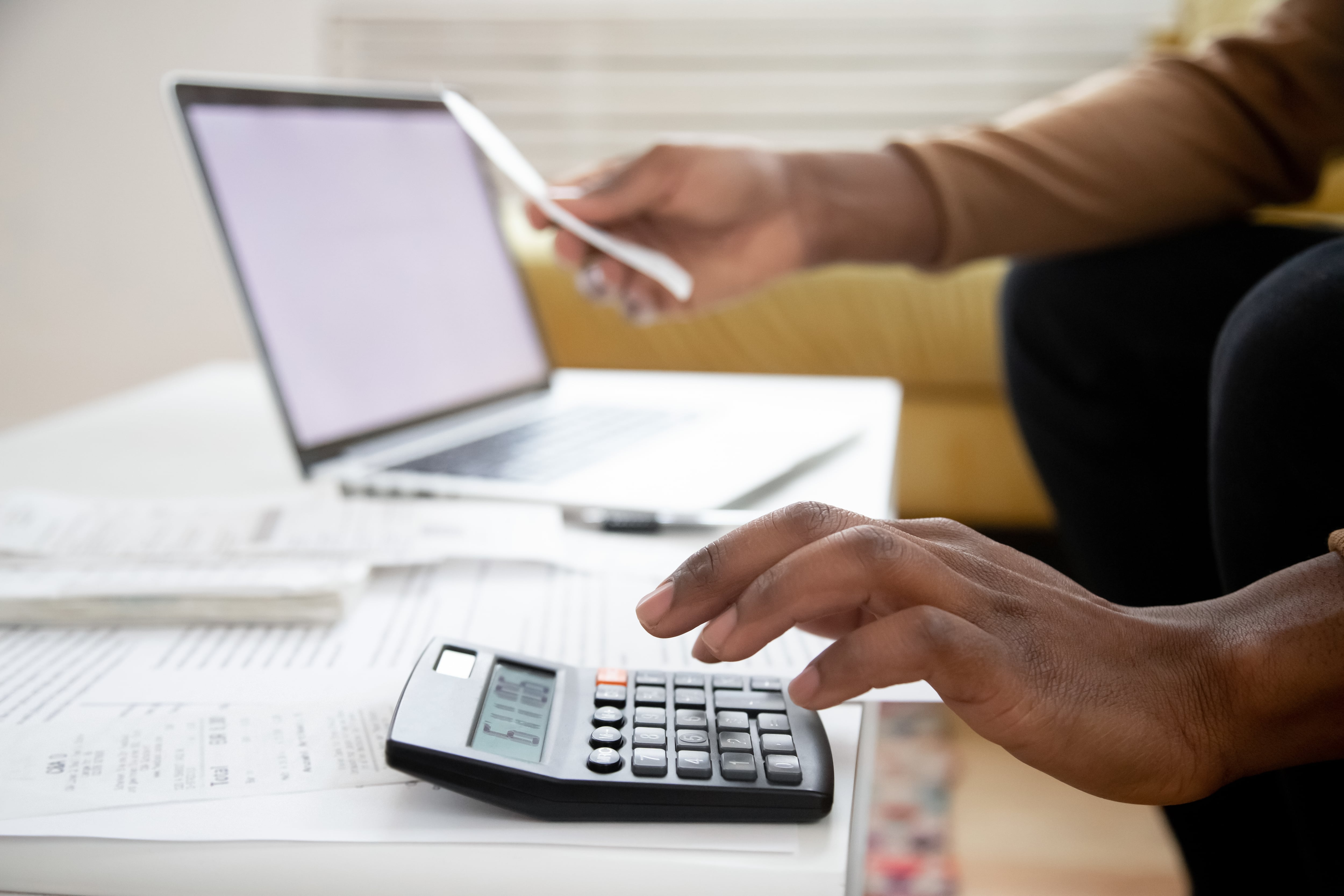 Mano de una persona utilizando una calculadora sobre una mesa con documentos y una computadora portátil en el fondo, representando el cálculo del impuesto anual para personas jurídicas en Costa Rica.