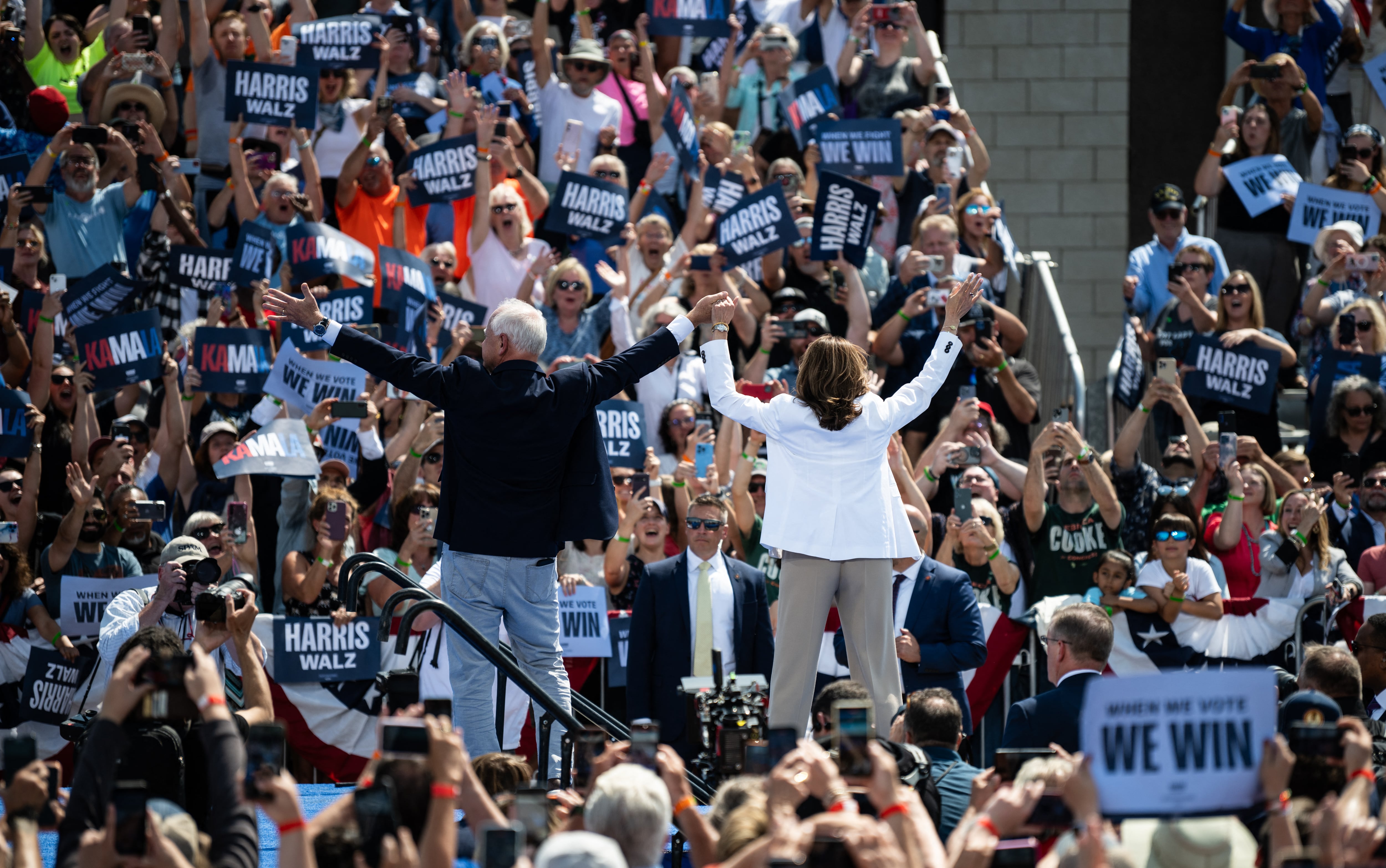 La candidata presidencial demócrata, vicepresidenta de Estados Unidos, Kamala Harris (derecha) y el candidato demócrata a la vicepresidencia, gobernador de Minnesota, Tim Walz (izquierda), se toman de la mano y saludan a la multitud en el escenario durante un mitin de campaña el 7 de agosto de 2024 en Eau Claire, Wisconsin