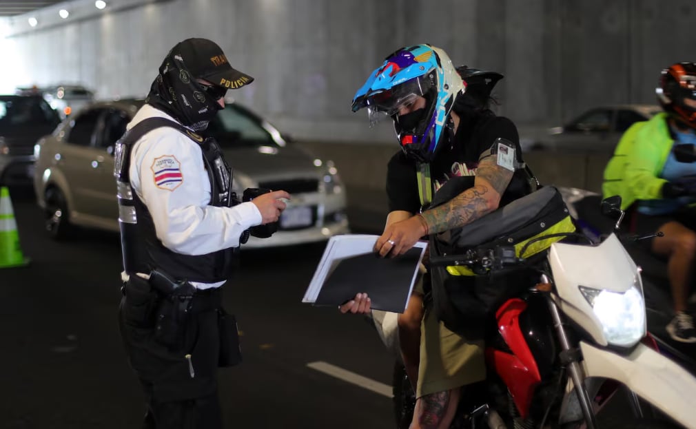 Un oficial de tránsito revisa la documentación de un motociclista en carretera.