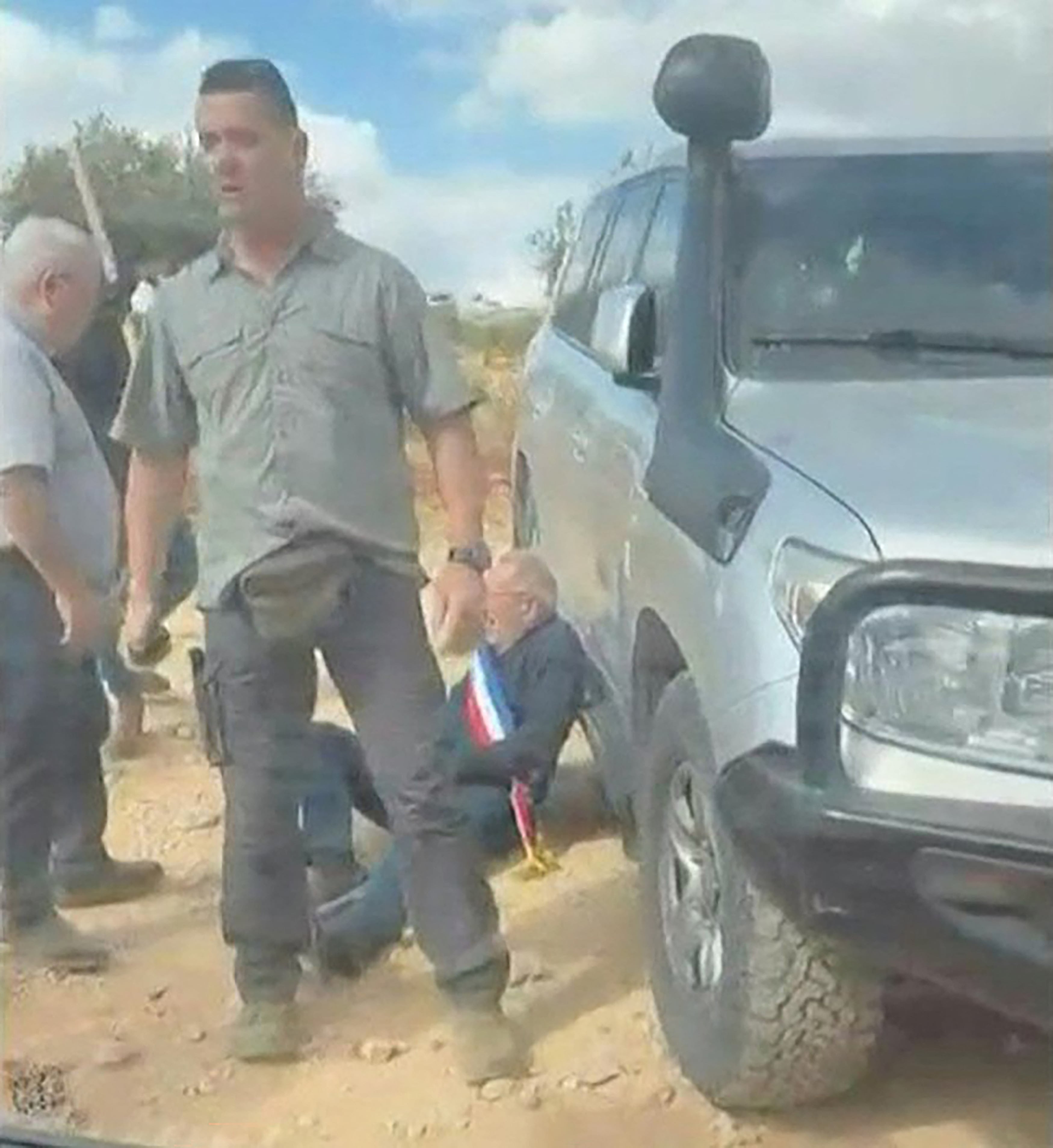 Esta captura de pantalla, tomada de material audiovisual generado por usuarios (UGC) obtenido el 17 de octubre de 2026, muestra a un hombre que lleva una banda de colores azul, blanco y rojo —del tipo que utilizan los funcionarios públicos franceses— apoyado contra un vehículo, mientras varios hombres enmascarados interceptan y rodean un automóvil en el que viajaban activistas, en la localidad cristiana de Taybeh, en Cisjordania (territorio bajo ocupación israelí). Bernard Baudoux, alcalde de la localidad francesa de Aulnoye-Aymeries (norte de Francia) —quien fue agredido el 17 de octubre de 2026 por colonos israelíes durante una visita de buena voluntad a la localidad palestina de Taybeh—, declaró a la AFP que el incidente demuestra que el gobierno derechista de Israel tolera la violencia de los colonos. (Foto: UGC / AFP) / PROHIBIDO SU USO DESPUÉS DEL 23 DE OCTUBRE DE 2026 A LAS 22:00:00 GMT - PROHIBIDO SU USO DESPUÉS DEL 23 DE OCTUBRE DE 2026 A LAS 22:00:00 GMT - XGTY - USO EXCLUSIVAMENTE EDITORIAL - CRÉDITO OBLIGATORIO: AFP PHOTO / UGC / AMIT ORFALI - PROHIBIDO SU USO EN CAMPAÑAS DE MARKETING O PUBLICIDAD - DISTRIBUIDO COMO SERVICIO A LOS CLIENTES - PROHIBIDO SU ARCHIVADO /