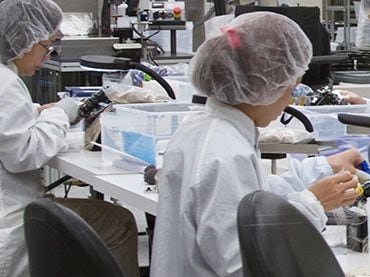 Operarios en una fábrica en Costa Rica trabajando en una línea de ensamblaje de dispositivos médicos, con equipos especializados y uniformes de laboratorio.
