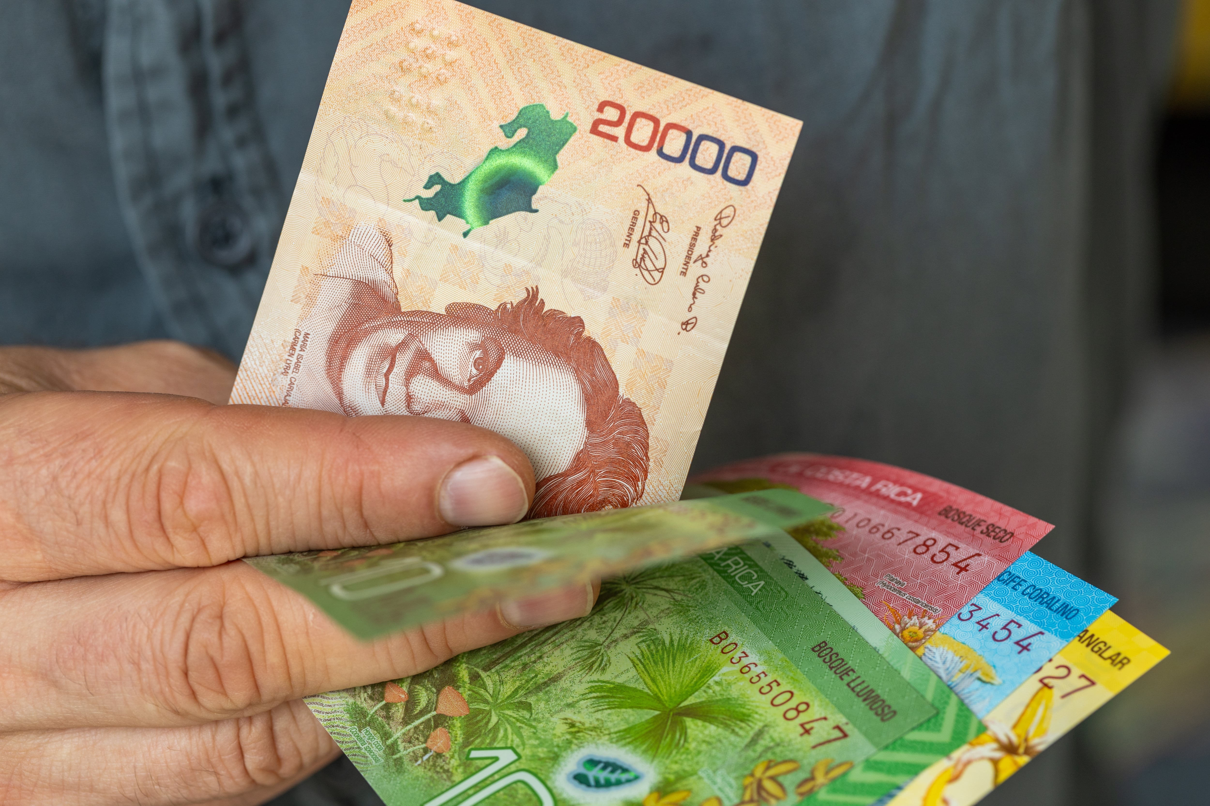 Mano sostiene varios billetes de colones costarricenses de distintas denominaciones, en referencia a los cambios en el gasto de consumo de los hogares según la Enigh 2024 y las variaciones entre quintiles de ingresos.