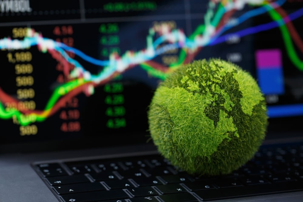 Un globo terráqueo verde de hojas y en el fondo una pantalla con gráficos de inversiones que crecen