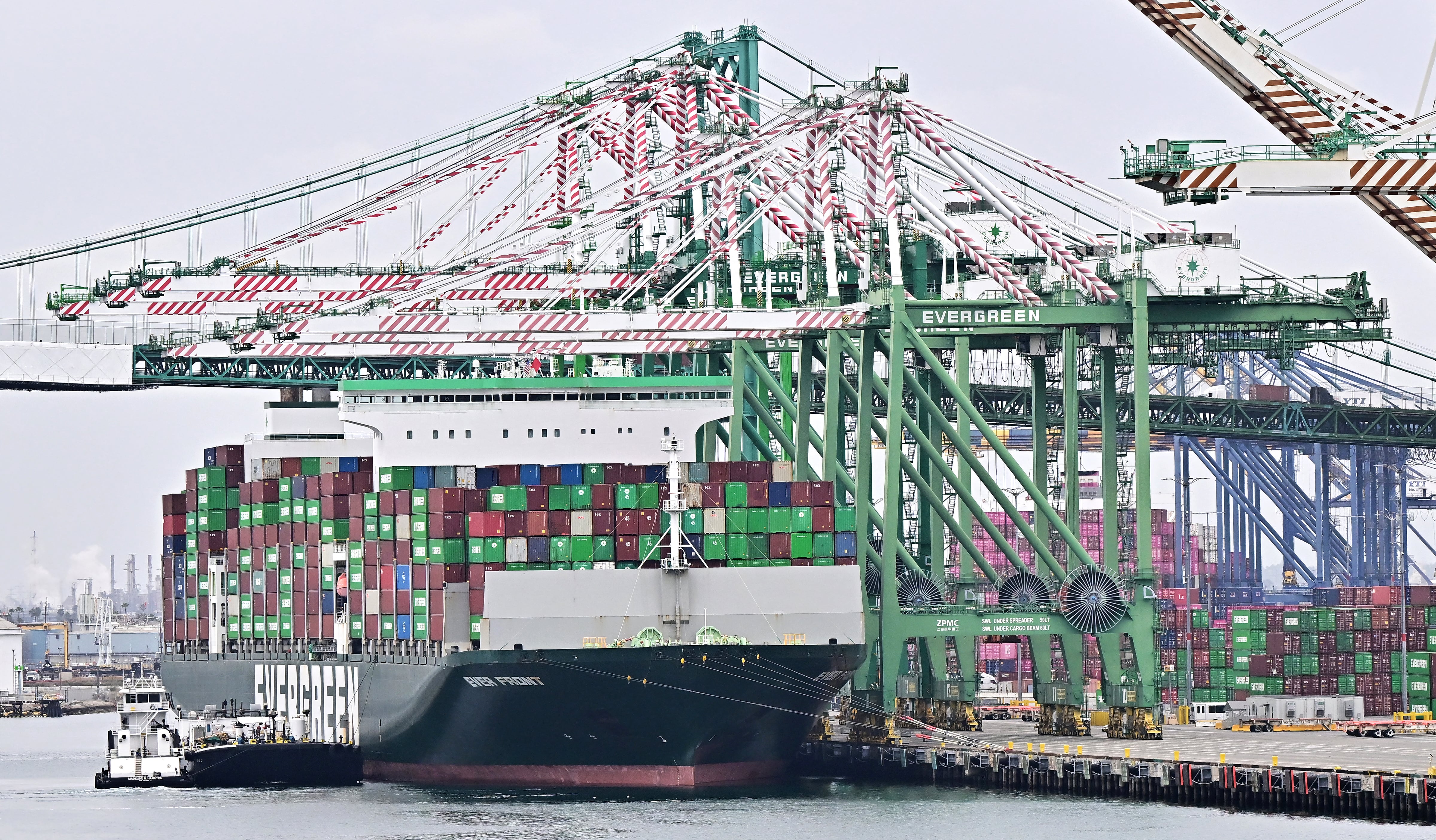 Un barco de carga de la compañía Evergreen, lleno de contenedores de colores, es operado por grúas en un puerto industrial, reflejando el comercio internacional y las exportaciones de México a EE.UU. bajo el T-MEC.