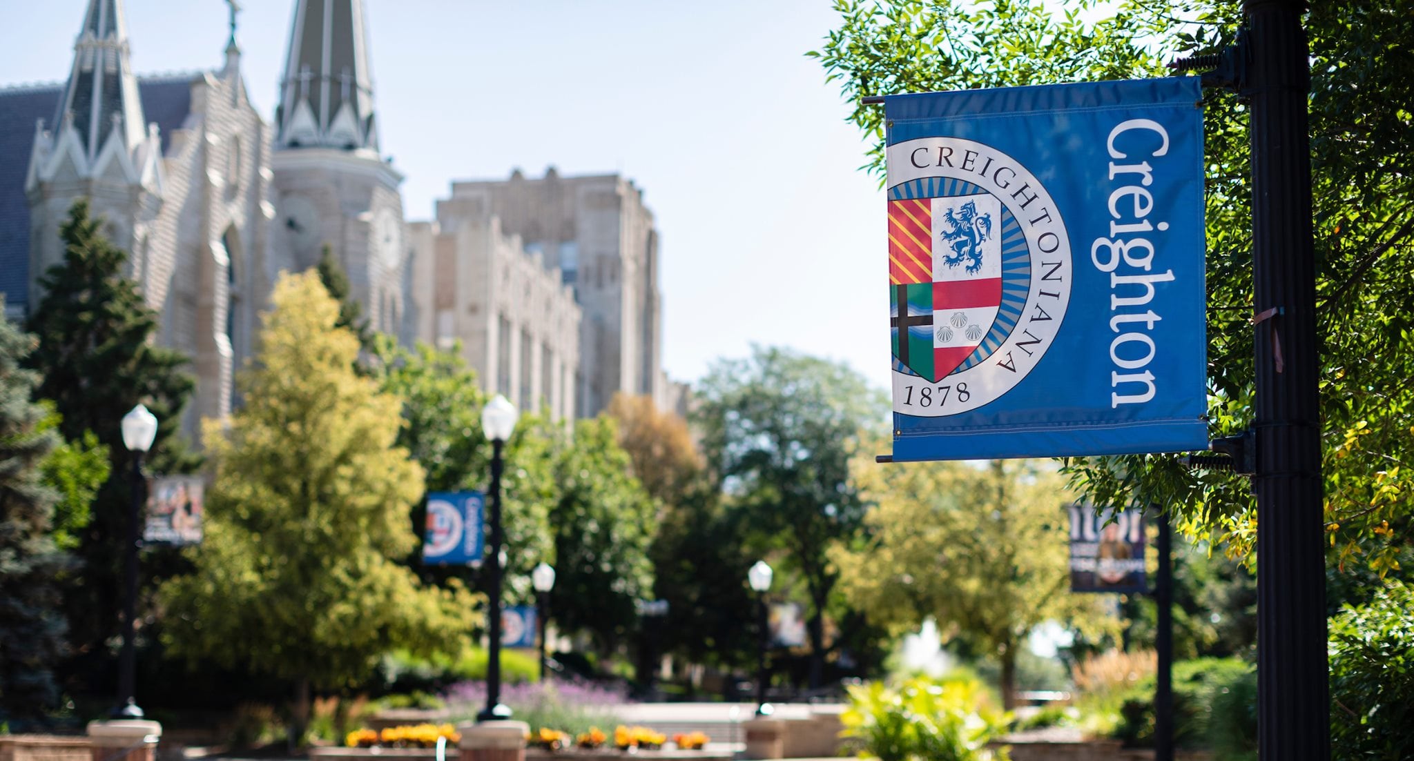 Imagen de una calle con vegetación a la derecha y a la izquierda un edificio antiguo, de dos o tres plantas.