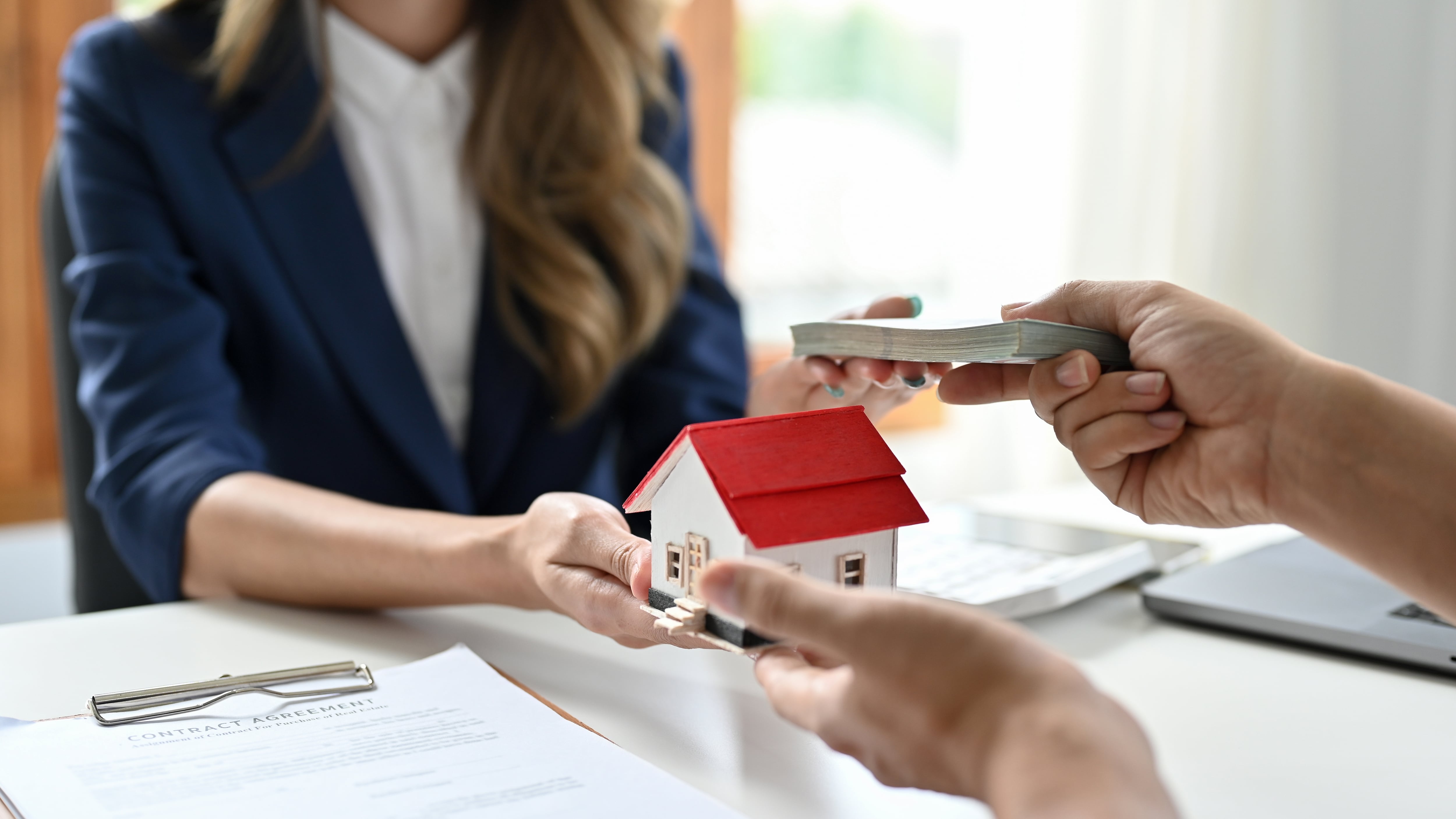 En la imagen una mujer intercambiando dinero y una casa
