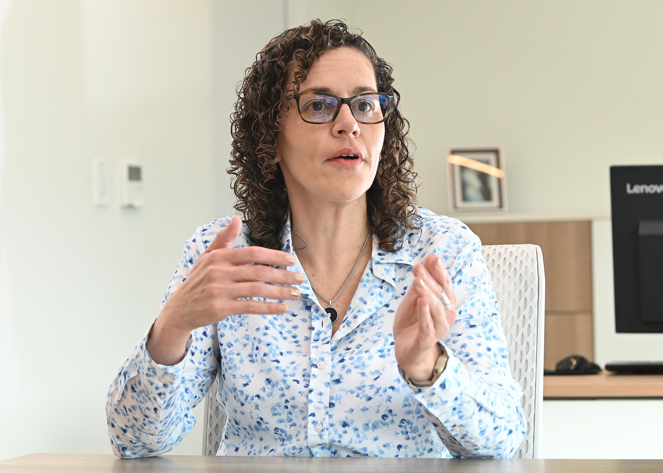 Hazel Valverde, superintendente de Sugef, gesticula mientras habla durante una entrevista en una oficina moderna, con un fondo que incluye una computadora y un cuadro en la pared.