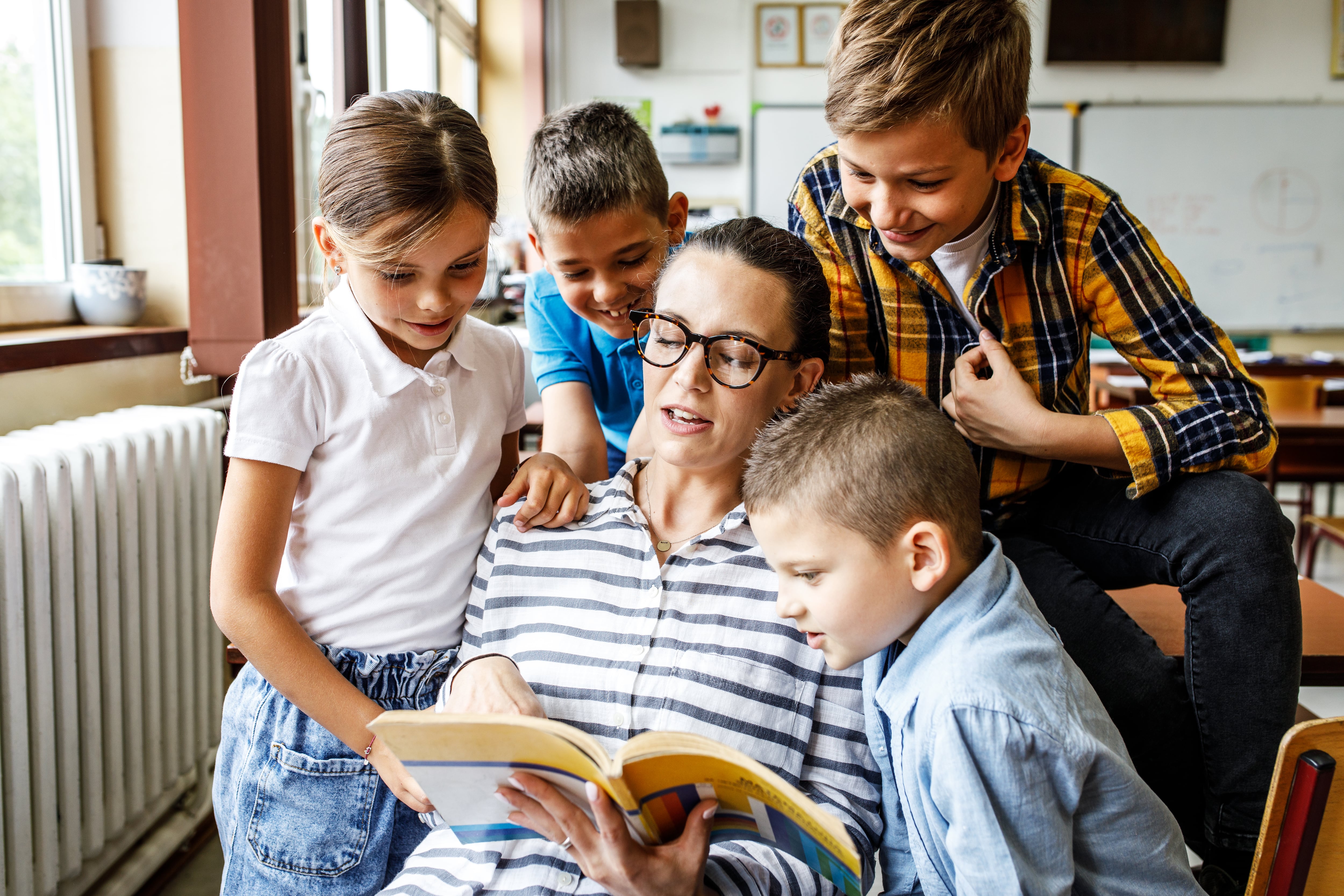 Maestra, docente, cuenta un cuento, lee un libro a cuatro de sus estudiantes, quienes la rodean