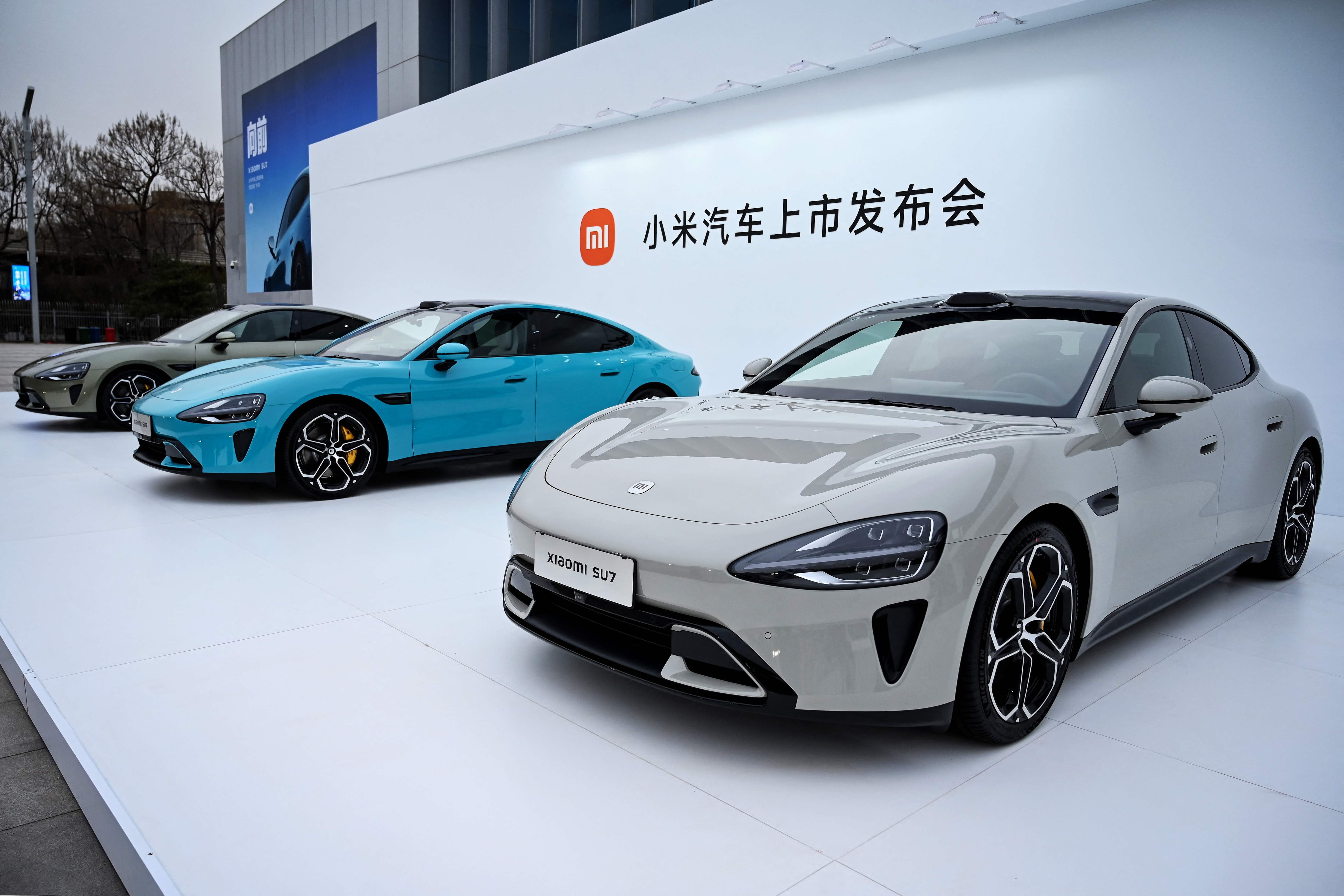 Tres vehículos eléctricos modelo Xiaomi SU7 en exhibición en un evento de lanzamiento en Pekín, reflejando la expansión de Xiaomi en el mercado de vehículos eléctricos en China.