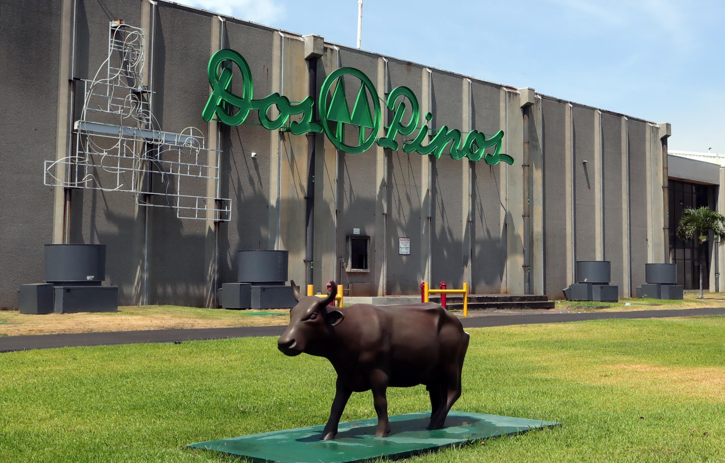 Fachada de la planta principal de Dos Pinos en Alajuela. Una estatua de una vaca en primer plano.