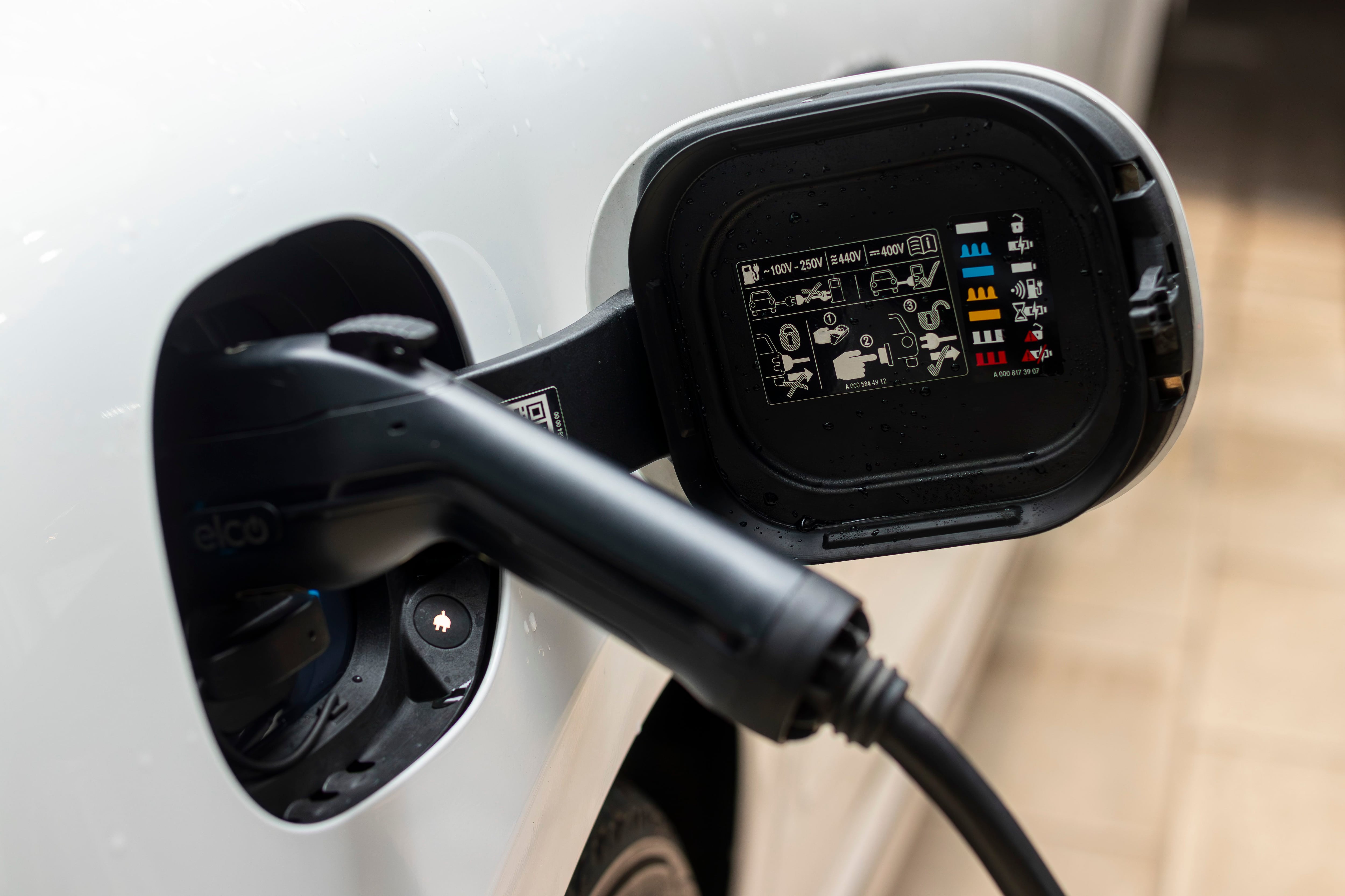 Puerto de carga de un vehículo eléctrico con el conector enchufado, mostrando etiquetas de especificaciones técnicas en el interior de la tapa.
