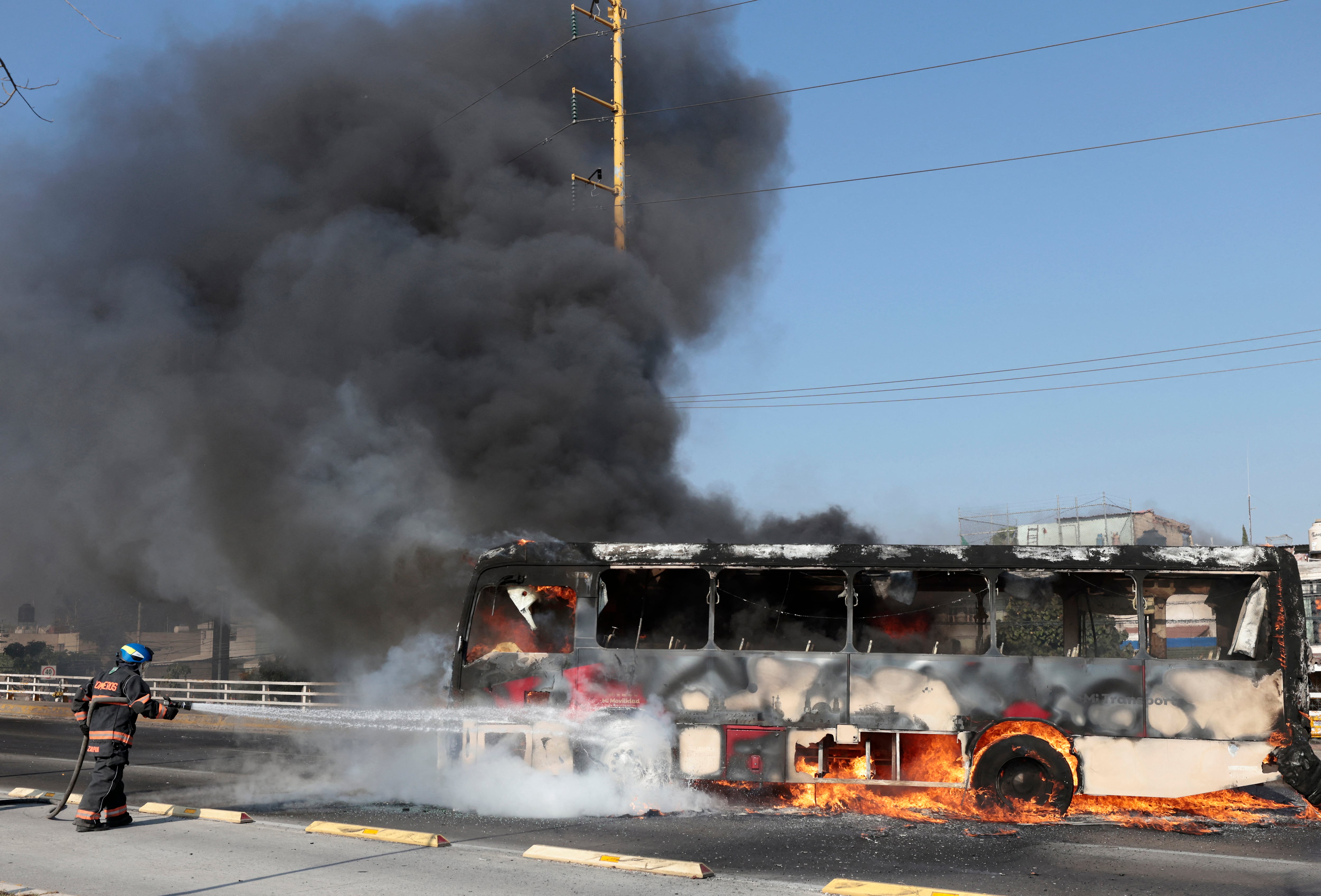 A firefighter extinguishes a burning bus set on fire by organised crime groups in response to an operation in Jalisco to arrest a high-priority security target, at one of the main avenues in Zapopan, state of Jalisco, Mexico, on February 22, 2026. Armed civilians blocked several roads in the state of Jalisco, in western Mexico, following an operation by federal forces in the town of Tapalpa, local authorities reported. Jalisco, which will host four matches of the upcoming 2026 World Cup, is home to the powerful Jalisco New Generation Cartel (CJNG), and has been rocked by several episodes of violence in recent years. (Photo by Ulises Ruiz / AFP)