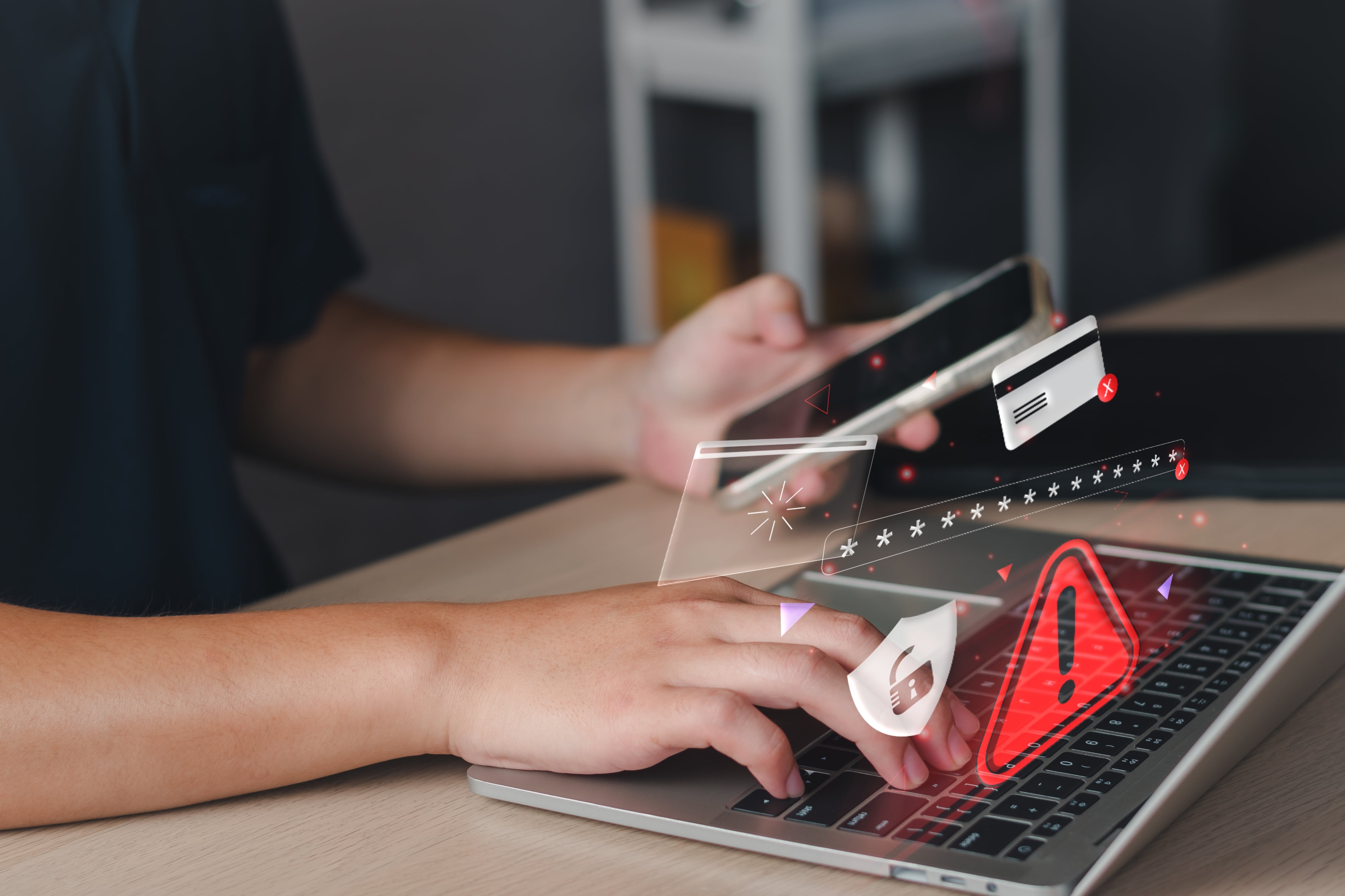 Persona utiliza computadora portátil y teléfono celular mientras se muestran íconos de alerta y seguridad digital, en alusión al proyecto de ley sobre estafas informáticas criticado por los bancos públicos de Costa Rica por el impacto en costos y responsabilidad financiera.